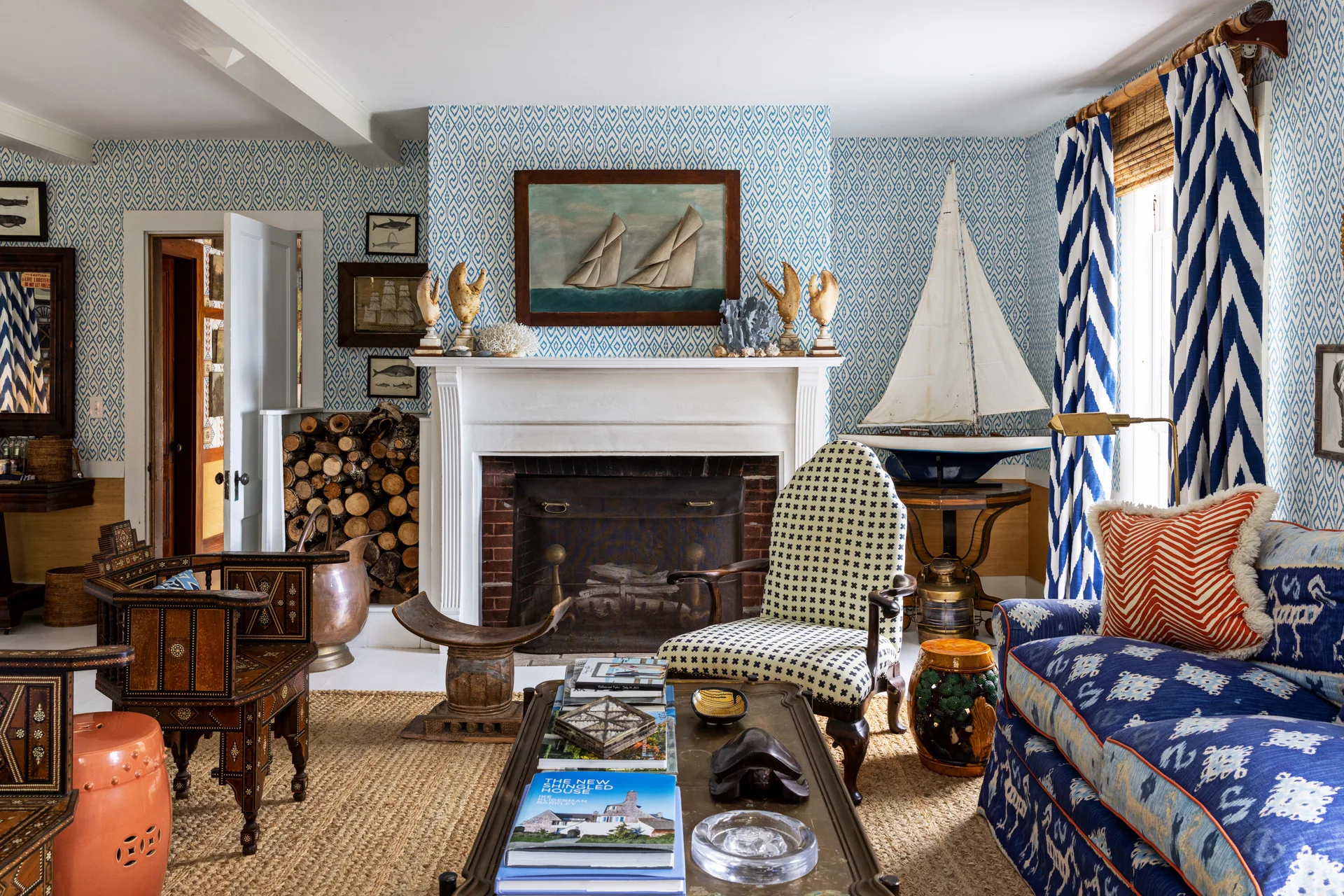 A living room features blue and white patterned wallpaper, a central white fireplace, a jute area rug, and an upholstered sofa with patterned pillows.