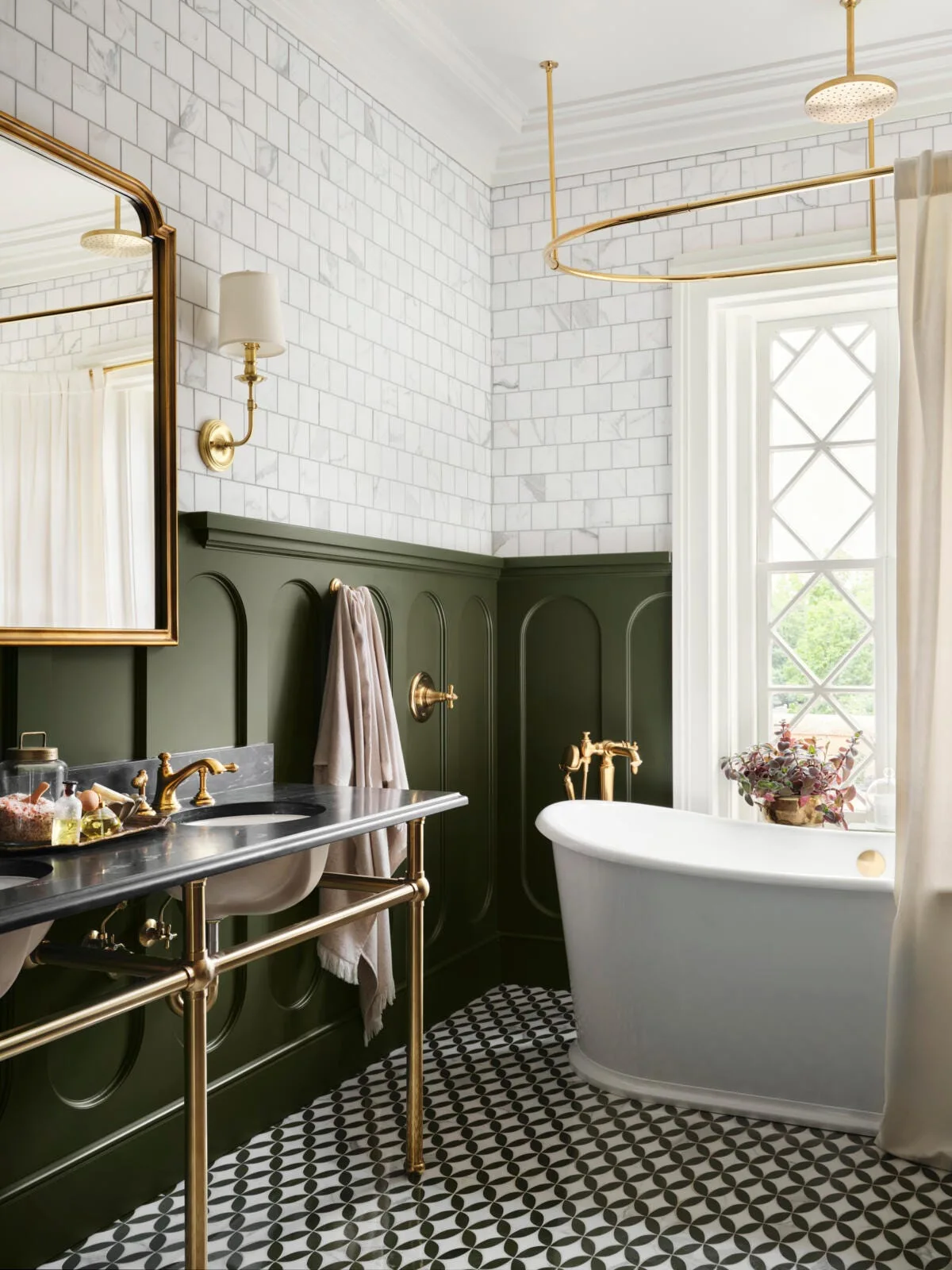 Traditional bathroom with forest green wainscoting, white subway tiles, a black marble console vanity, and a freestanding tub with brass fixtures.