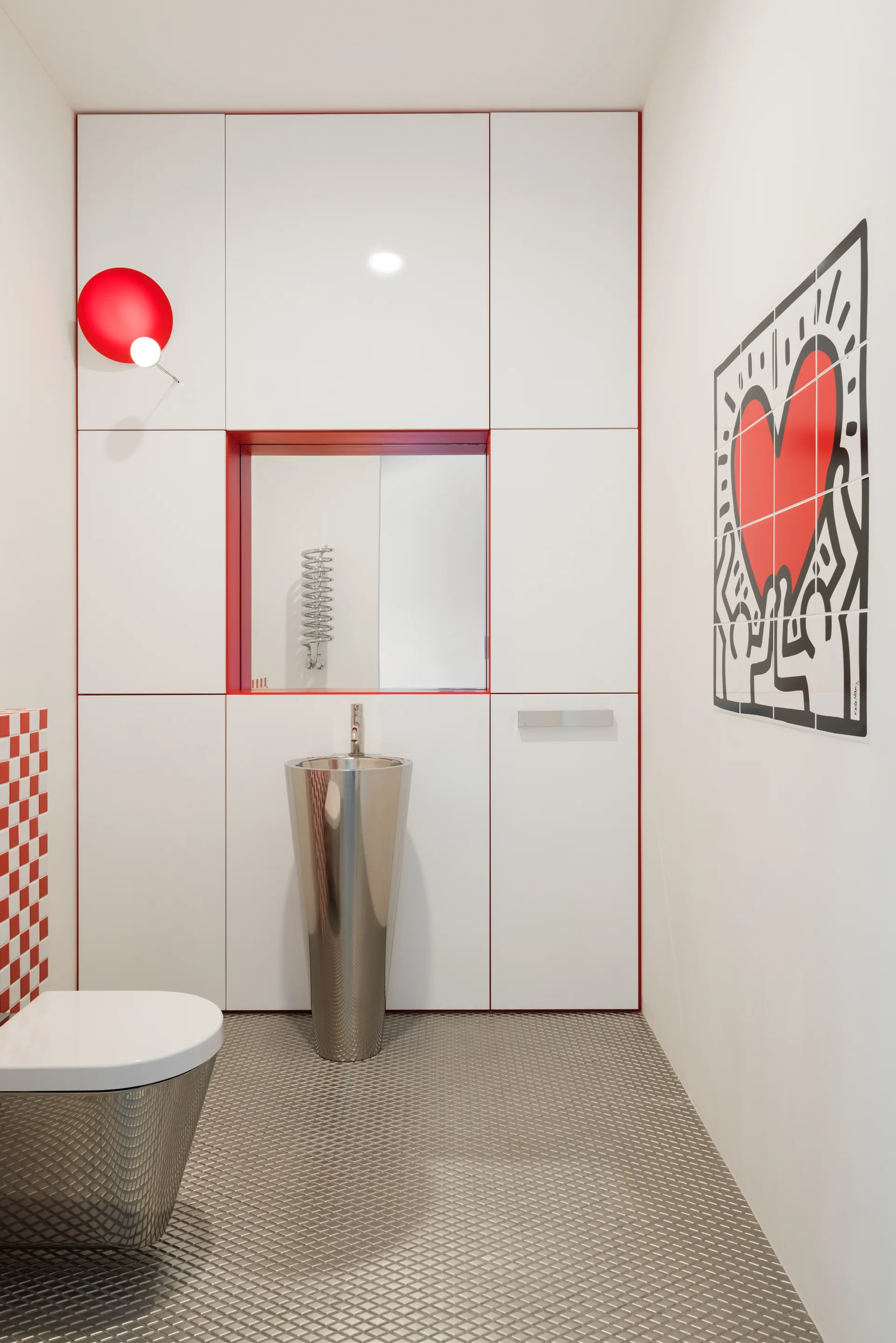 A modern powder room features a cone-shaped metallic sink, white high-gloss cabinetry with red trim, and textured silver diamond-plate flooring.