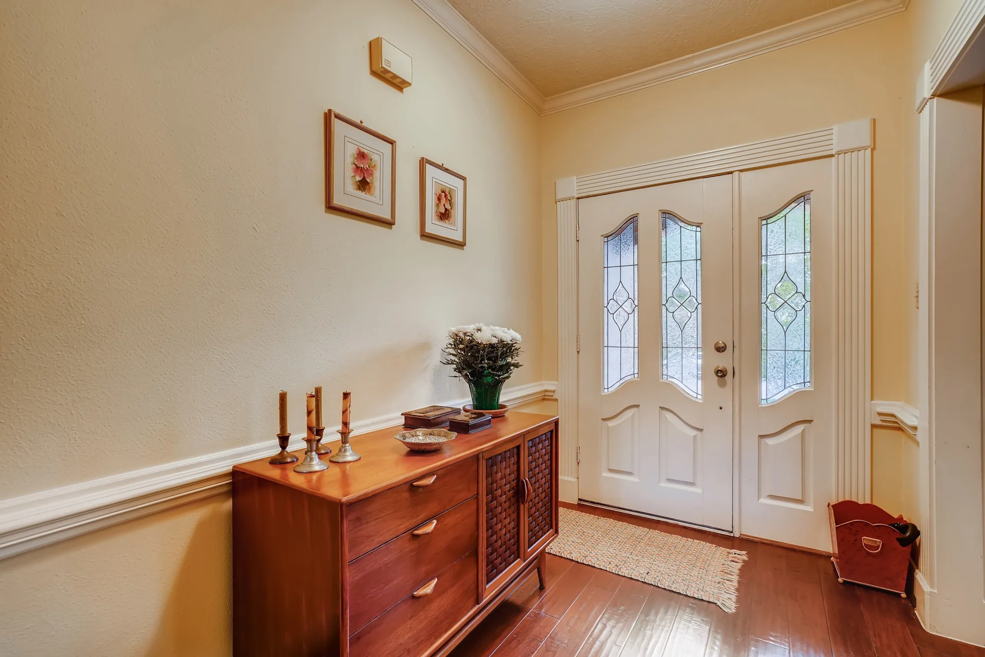 An entryway featuring a wooden mid-century credenza on dark wood floors next to a white front door with leaded glass panels.