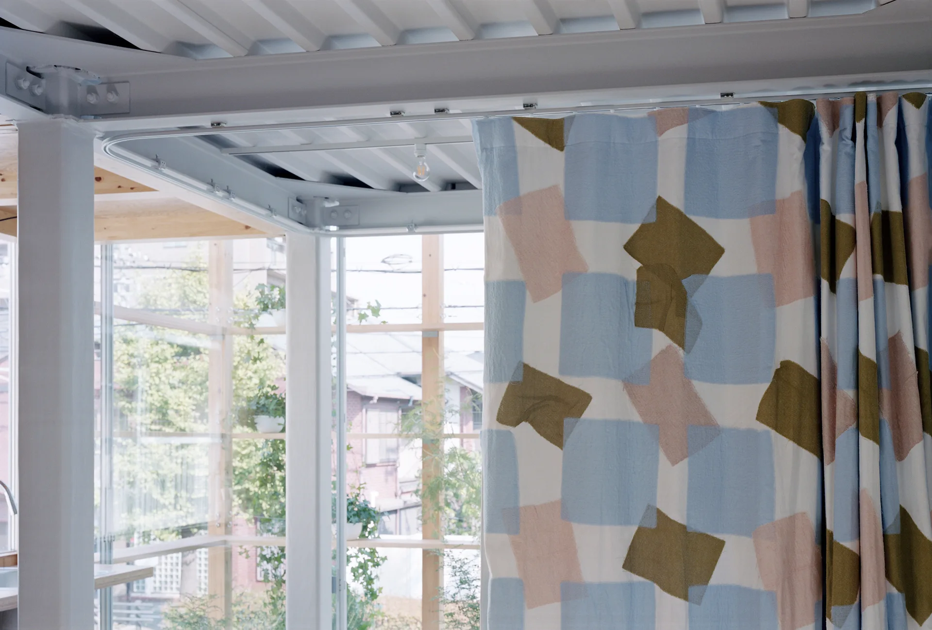 A pastel color-blocked curtain hangs from a ceiling-mounted track next to an exposed white steel beam and glass window.