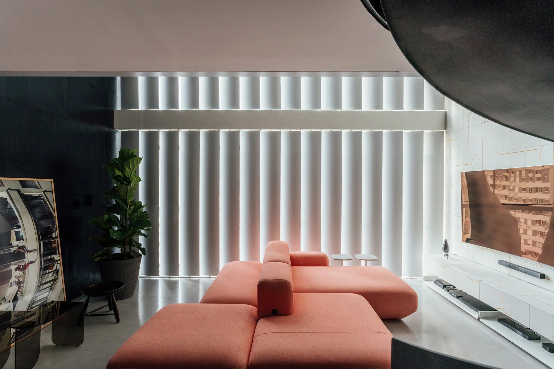 A contemporary living room featuring a peach modular sofa, floor-to-ceiling vertical blinds, and a white geometric wall with a TV.