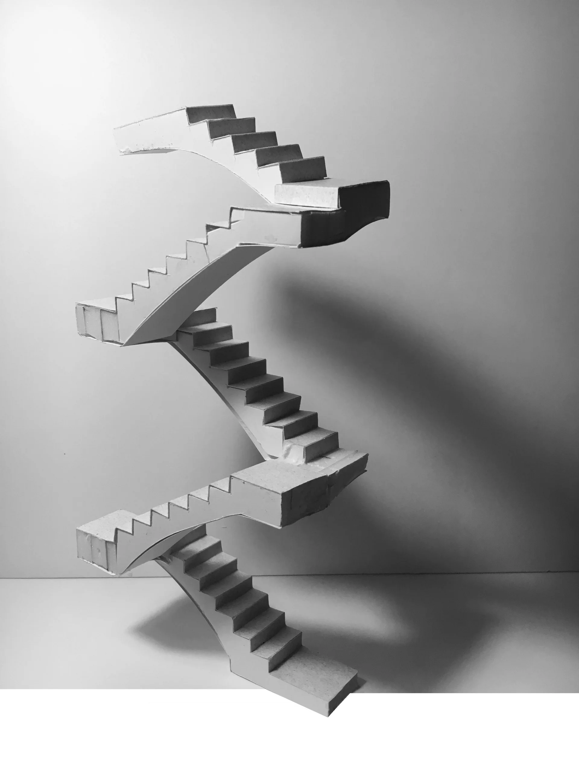A white paper architectural study model of a multi-level zigzag staircase casting a dark shadow against a plain background.