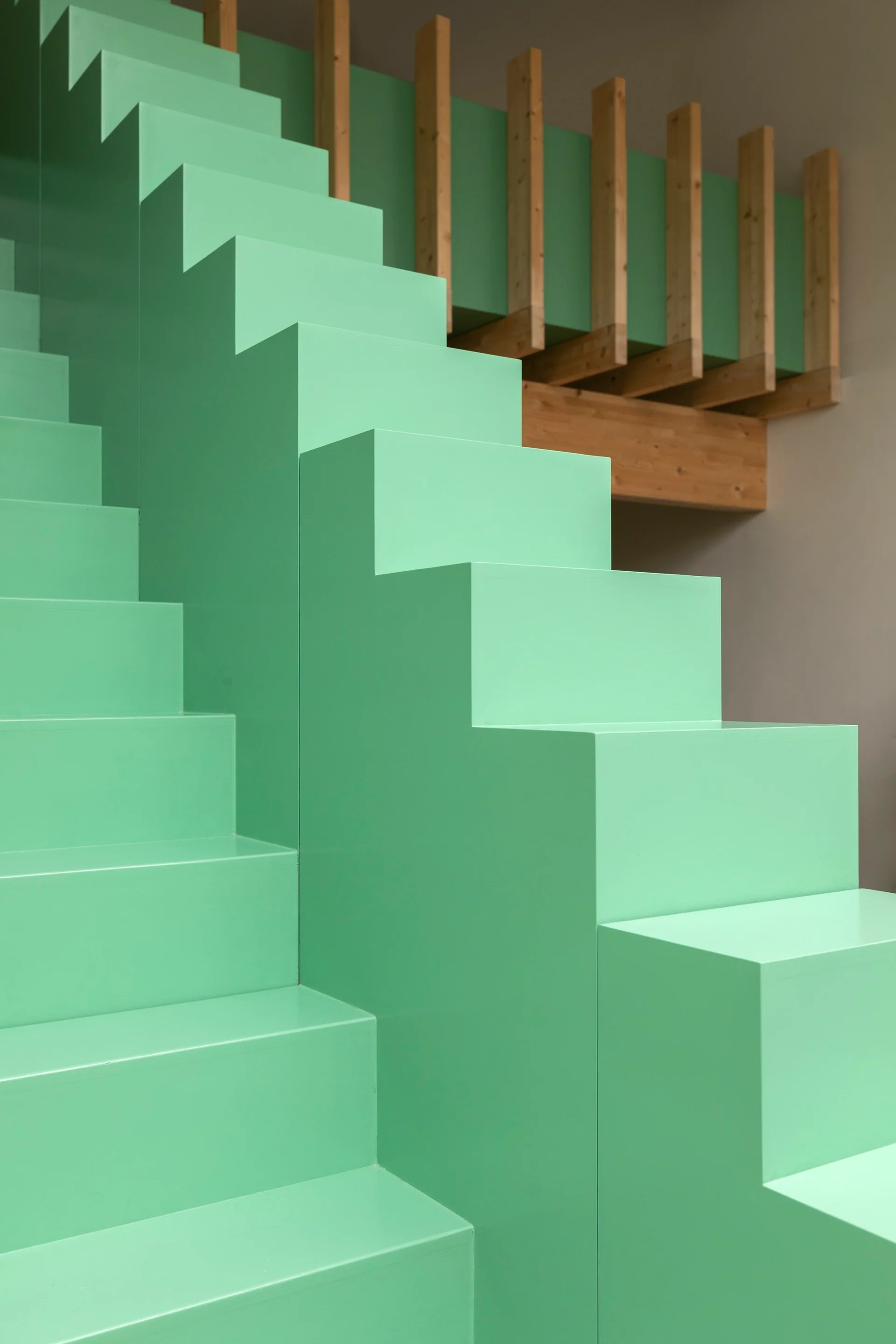 A minimalist mint green staircase with sharp geometric block steps ascends next to vertical wooden railing slats.