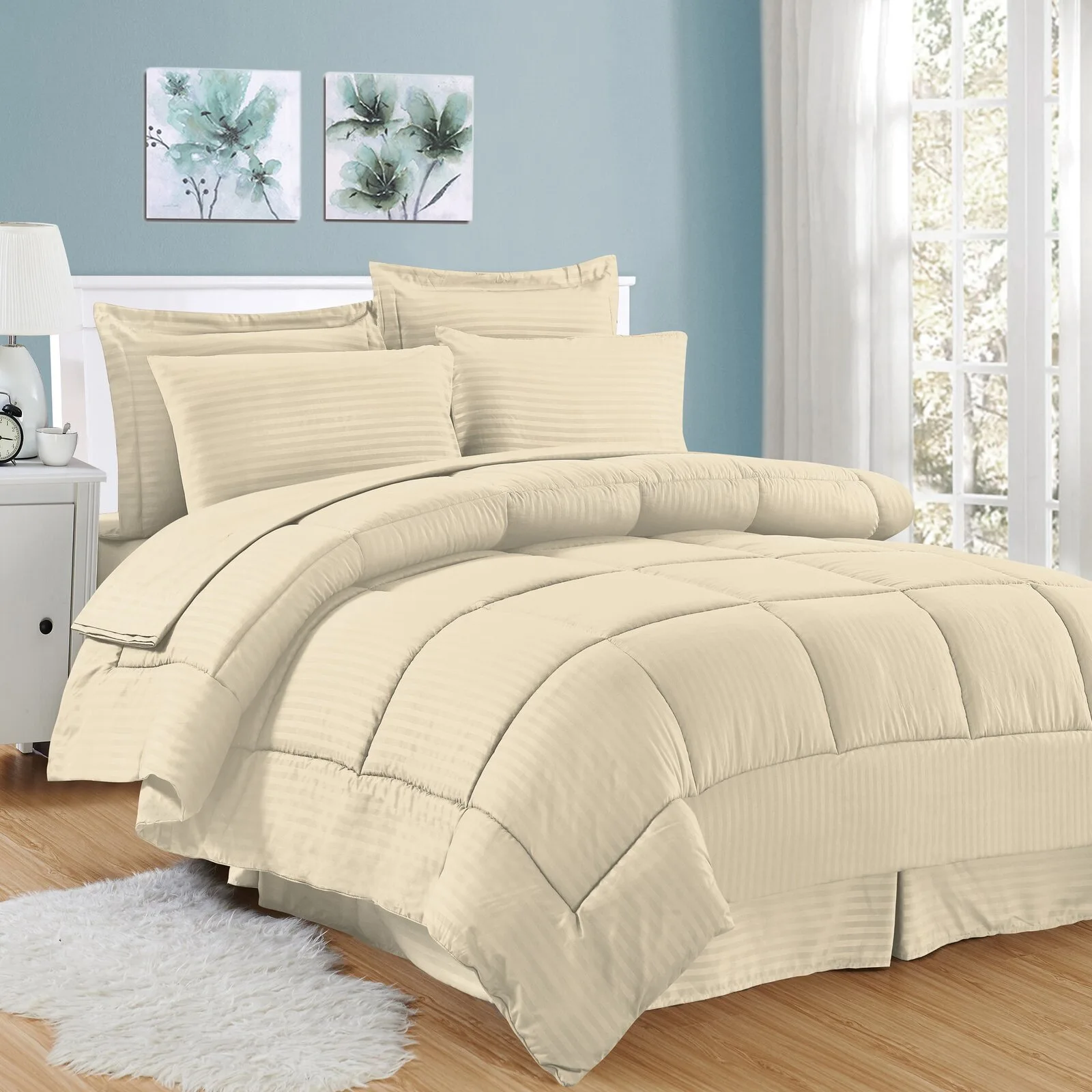 A bed made with beige striped bedding sits against a light blue wall decorated with two floral pictures on a light wood floor with a fluffy rug.