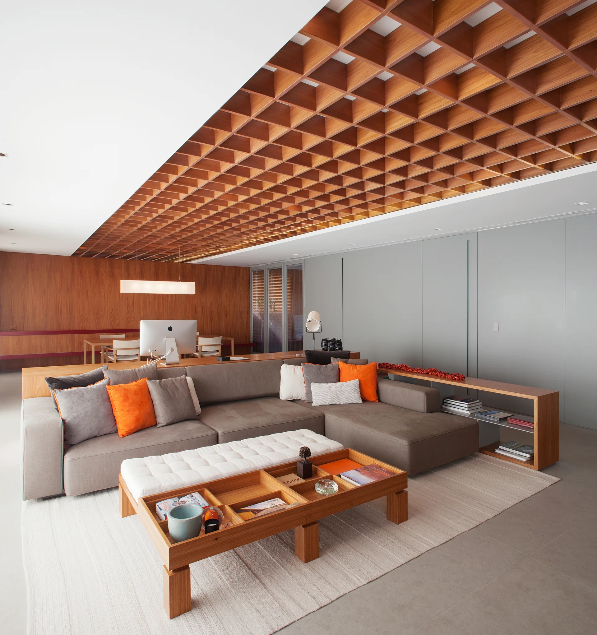 A modern living room features a grey sectional sofa, a compartmented wooden coffee table, and a wooden grid coffered ceiling.