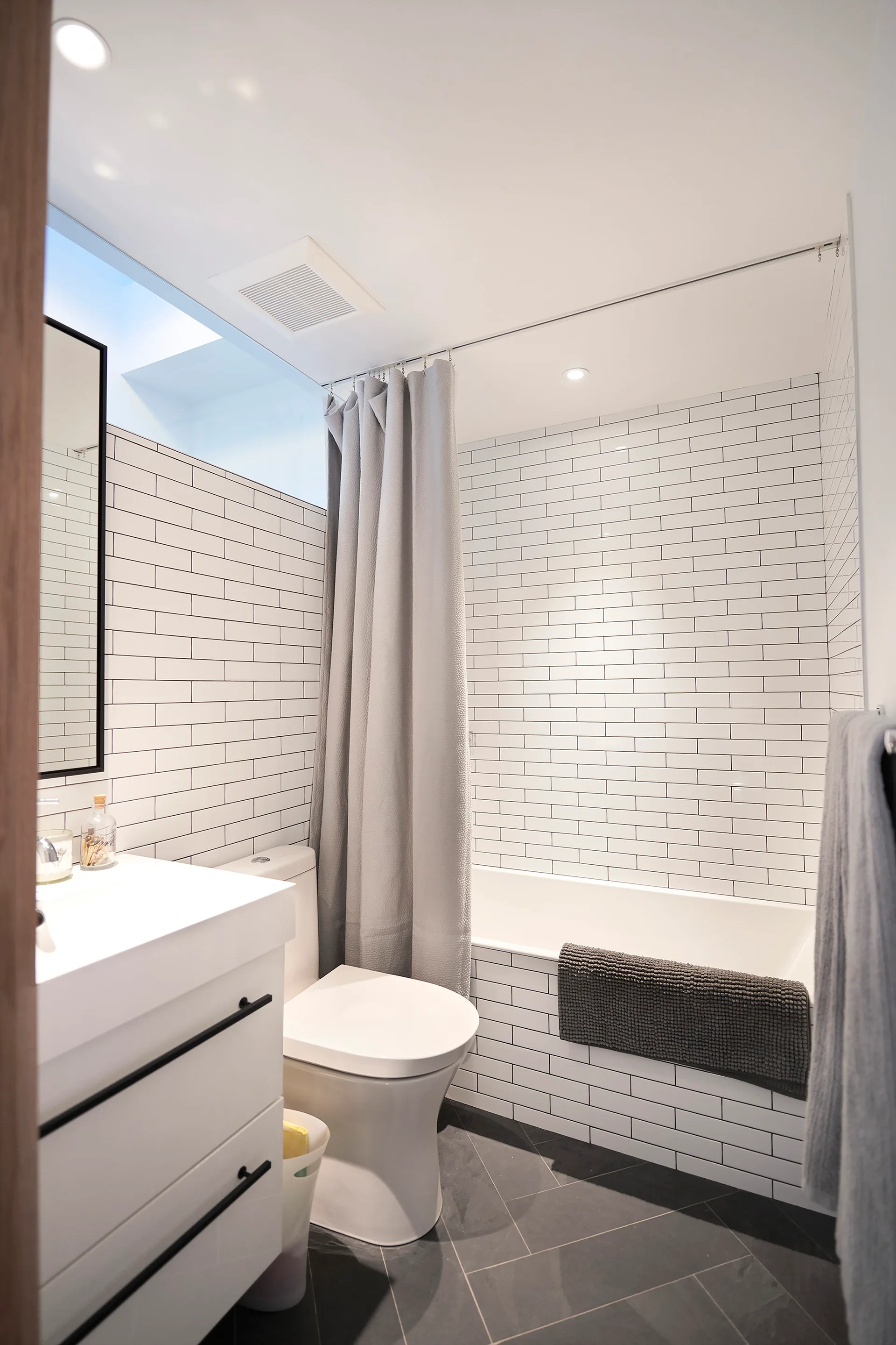 A minimalist bathroom features white subway tile walls, a white floating vanity, a modern toilet, and a grey shower curtain.