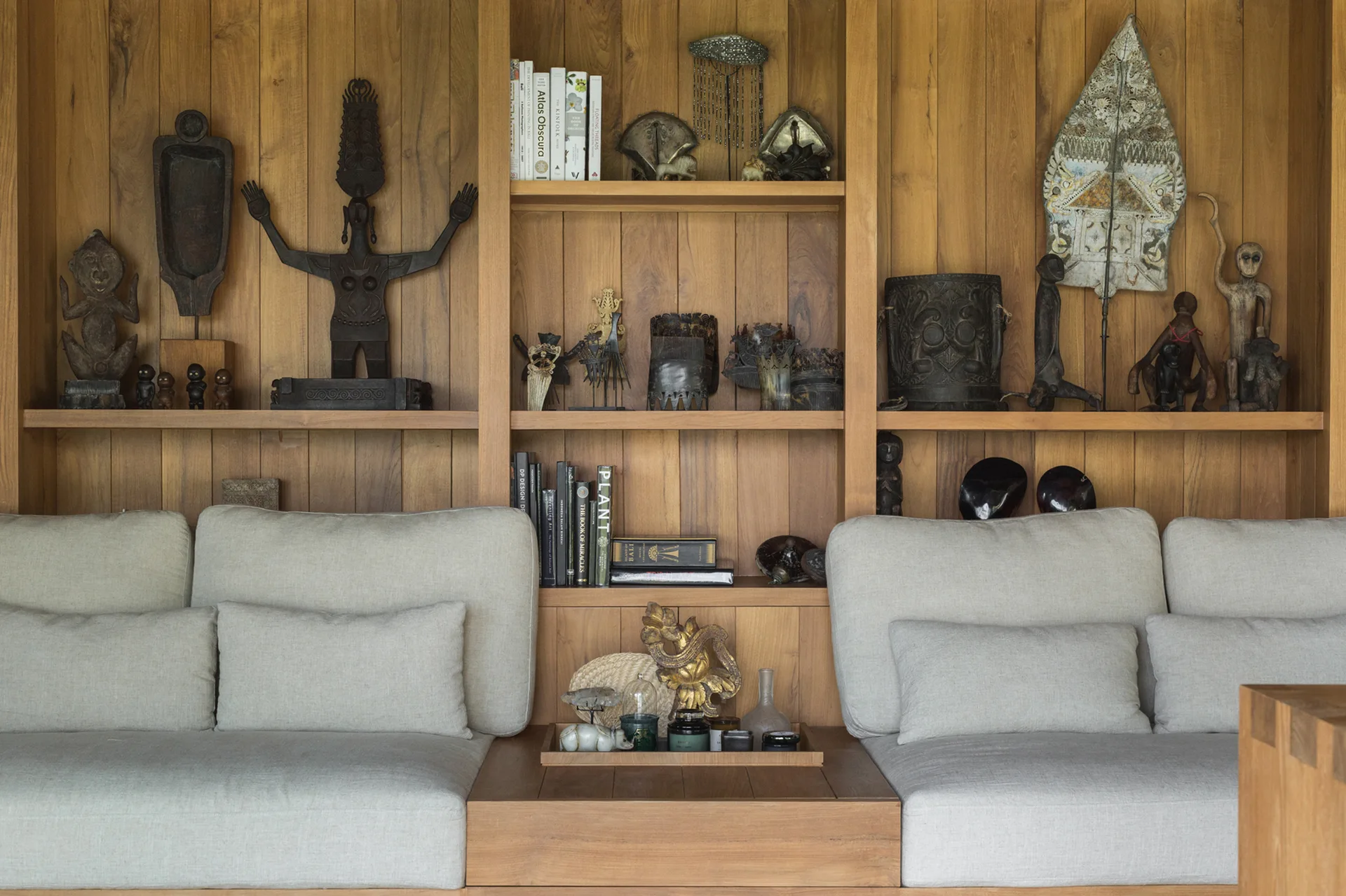 Upholstered beige sofa cushions set against a built-in wooden shelving unit filled with dark global sculptures and books.