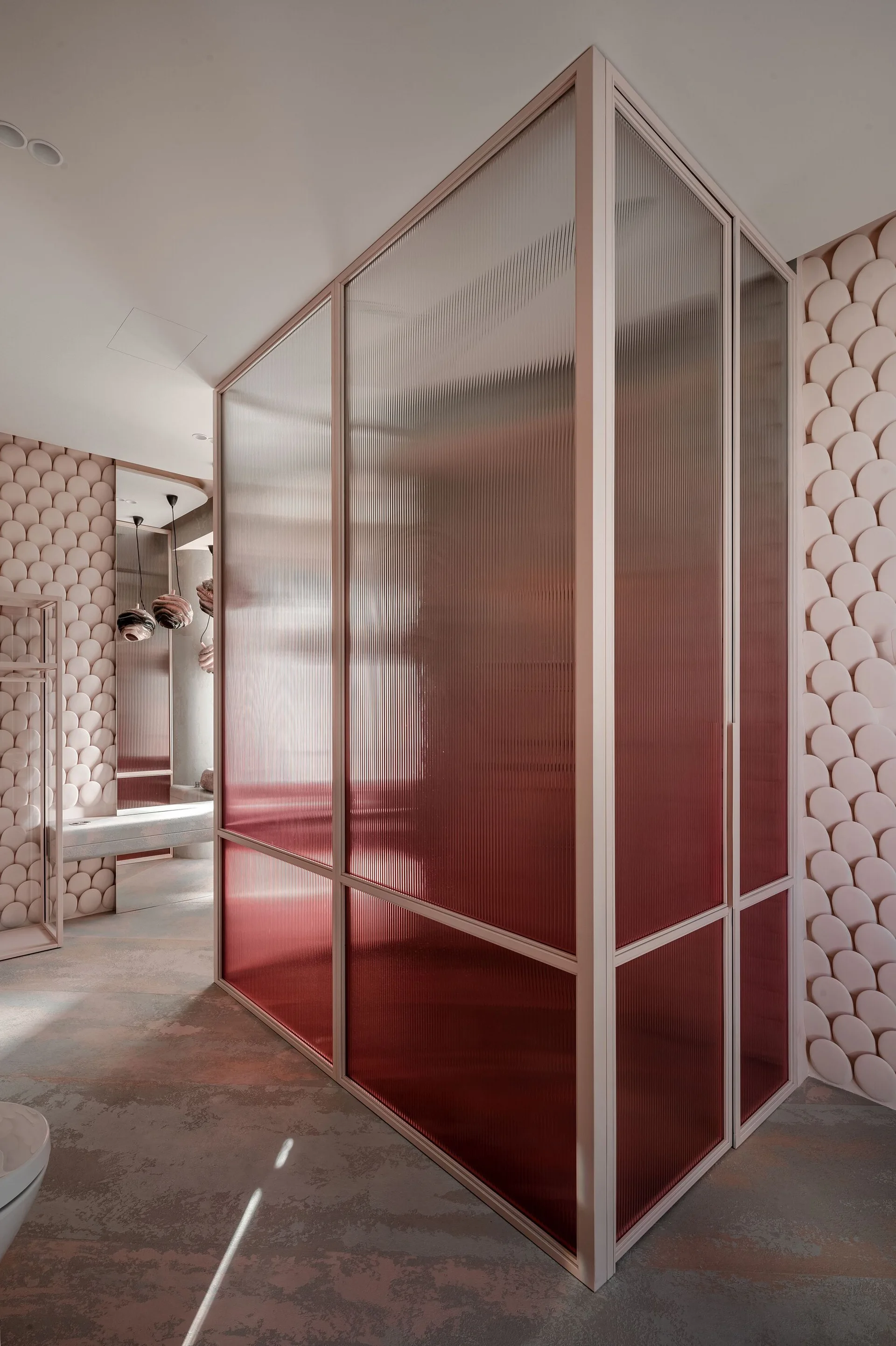 A modern bathroom features dusty rose scalloped wall panels, a fluted glass partition screen, and textured flooring.