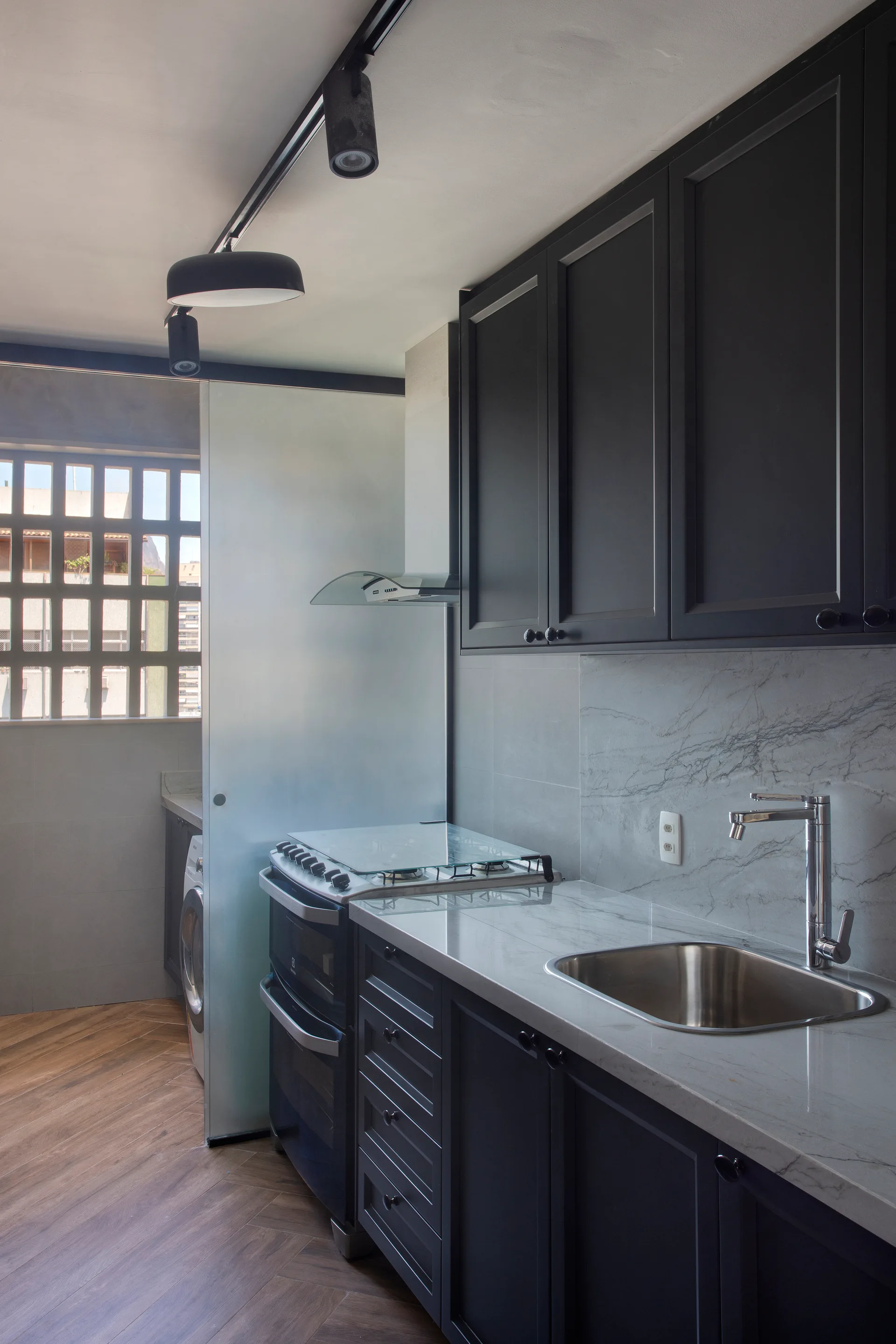 A compact kitchen features dark gray cabinetry, a marble-like countertop with a sink, and a frosted glass sliding partition door.