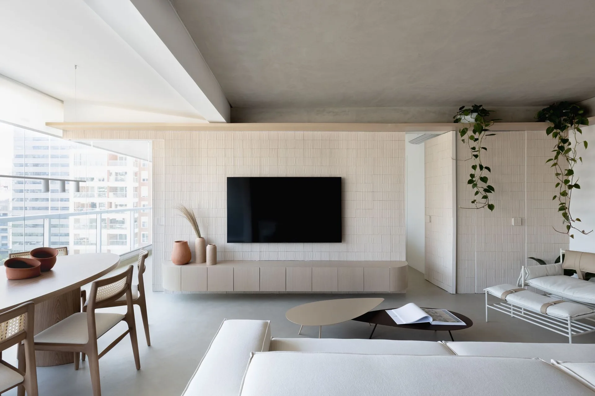 An open-concept living room features a textured fluted accent wall with a mounted television, a floating beige console, and a wooden dining set.