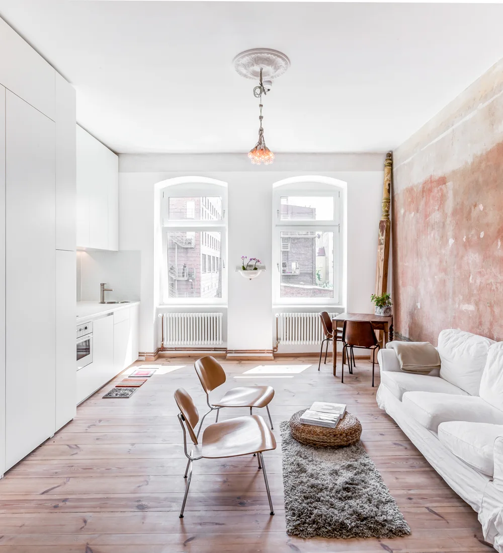 An open-concept living area and kitchen featuring a white slipcovered sofa, a distressed terracotta accent wall, and two molded plywood chairs.