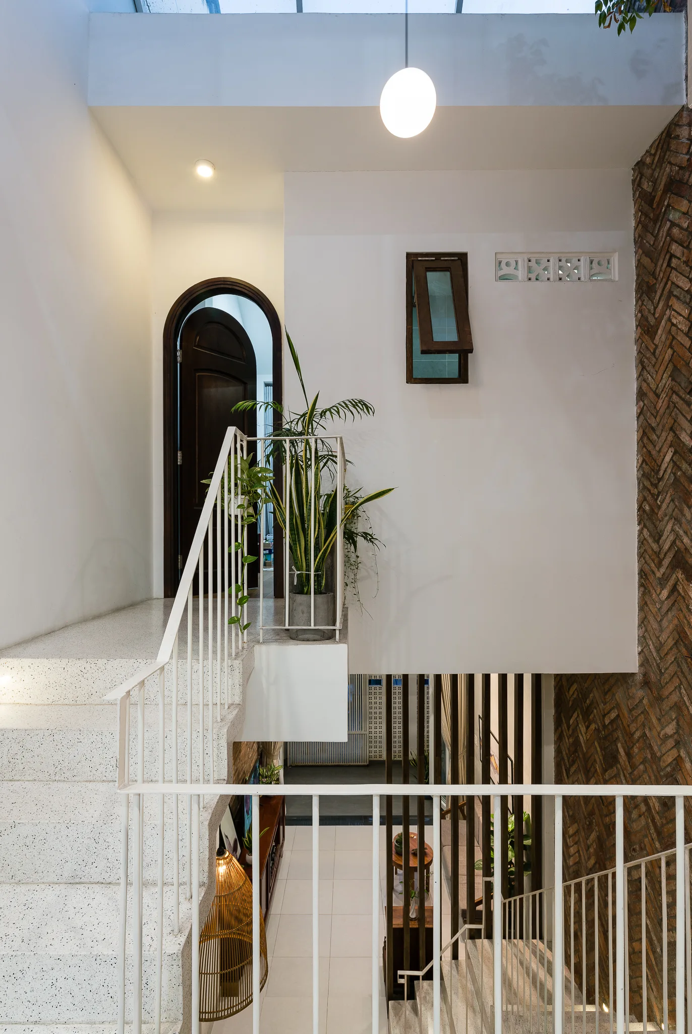 A multi-level staircase with terrazzo treads and thin white metal railings runs alongside a textured herringbone brick wall beneath an arched wooden doorway.