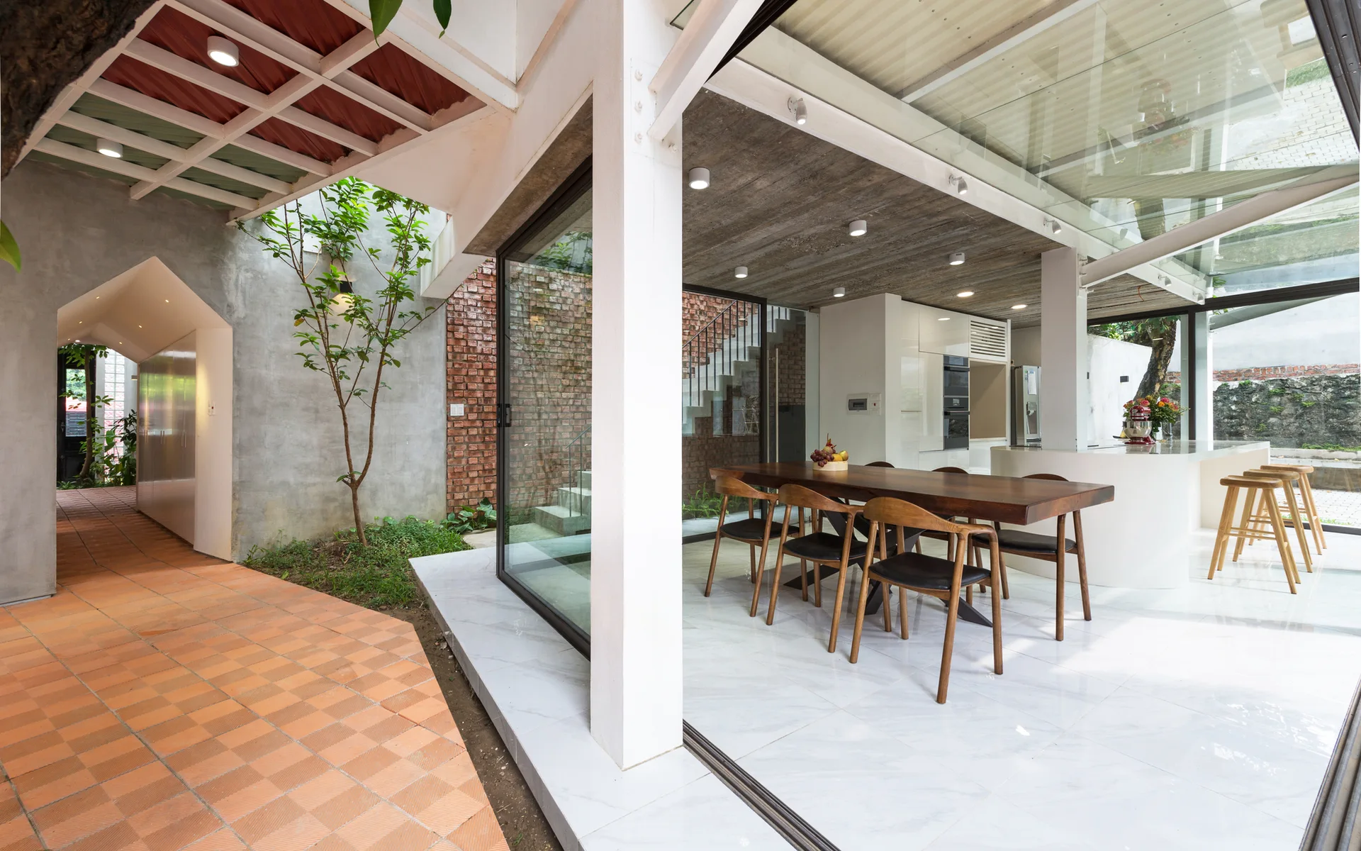 A modern open-plan dining room with a dark wood table features a raw concrete ceiling and large sliding glass doors opening to a courtyard.