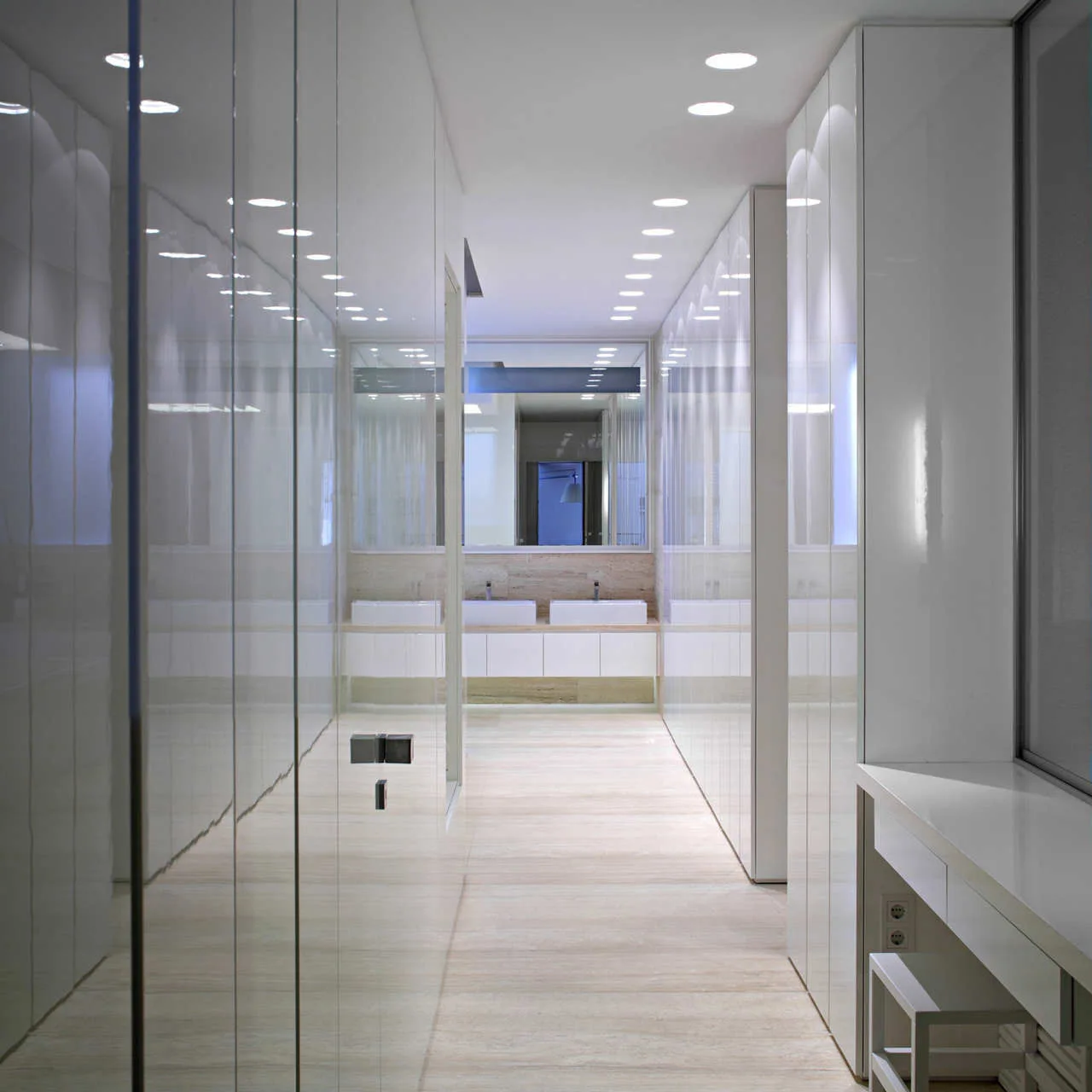 A long, minimalist white bathroom hallway with reflective high-gloss wall panels, natural stone floors, and a double vanity at the far end.