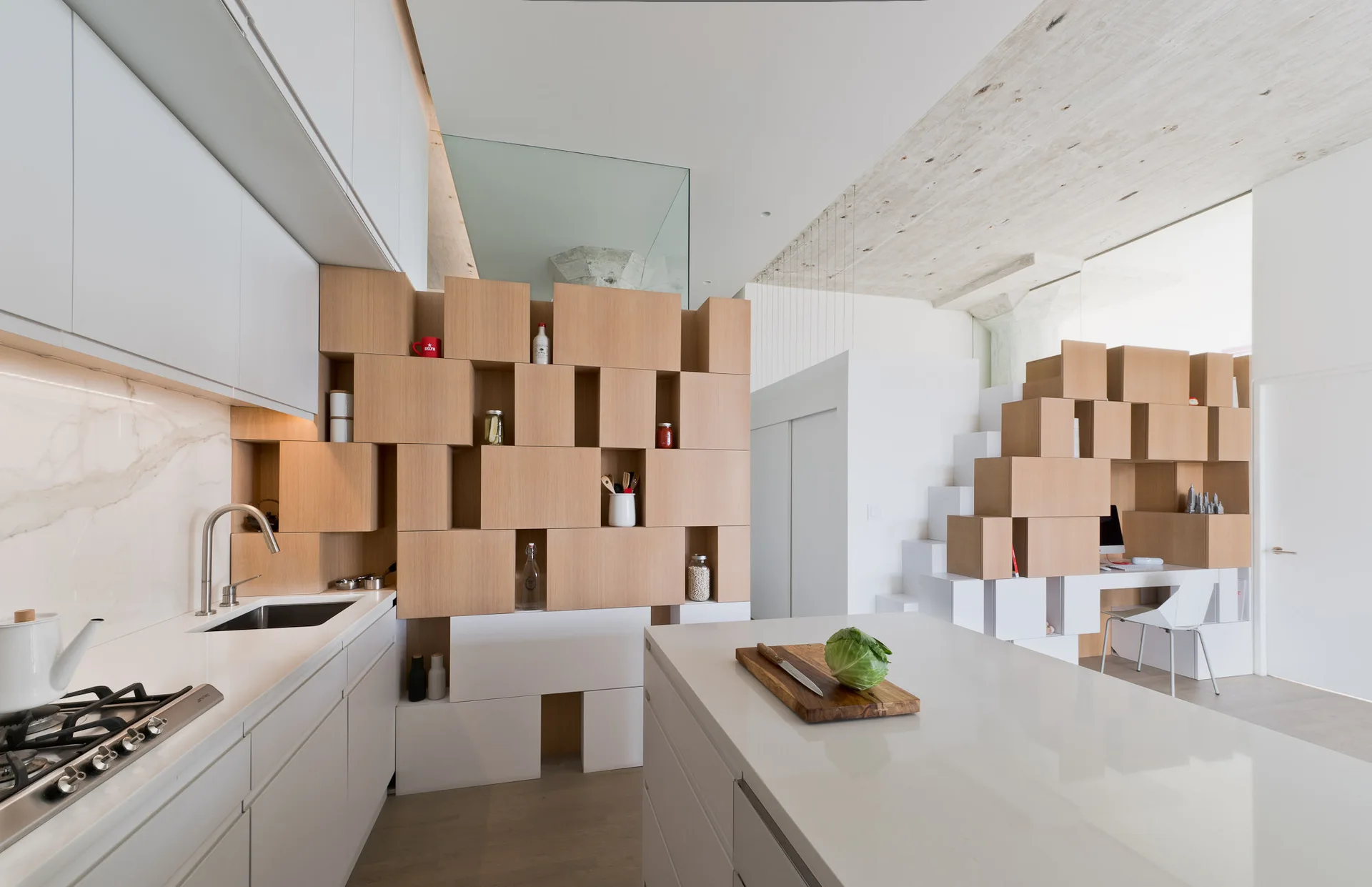 A modern kitchen with white cabinetry and an island next to a modular light wood cube partition.