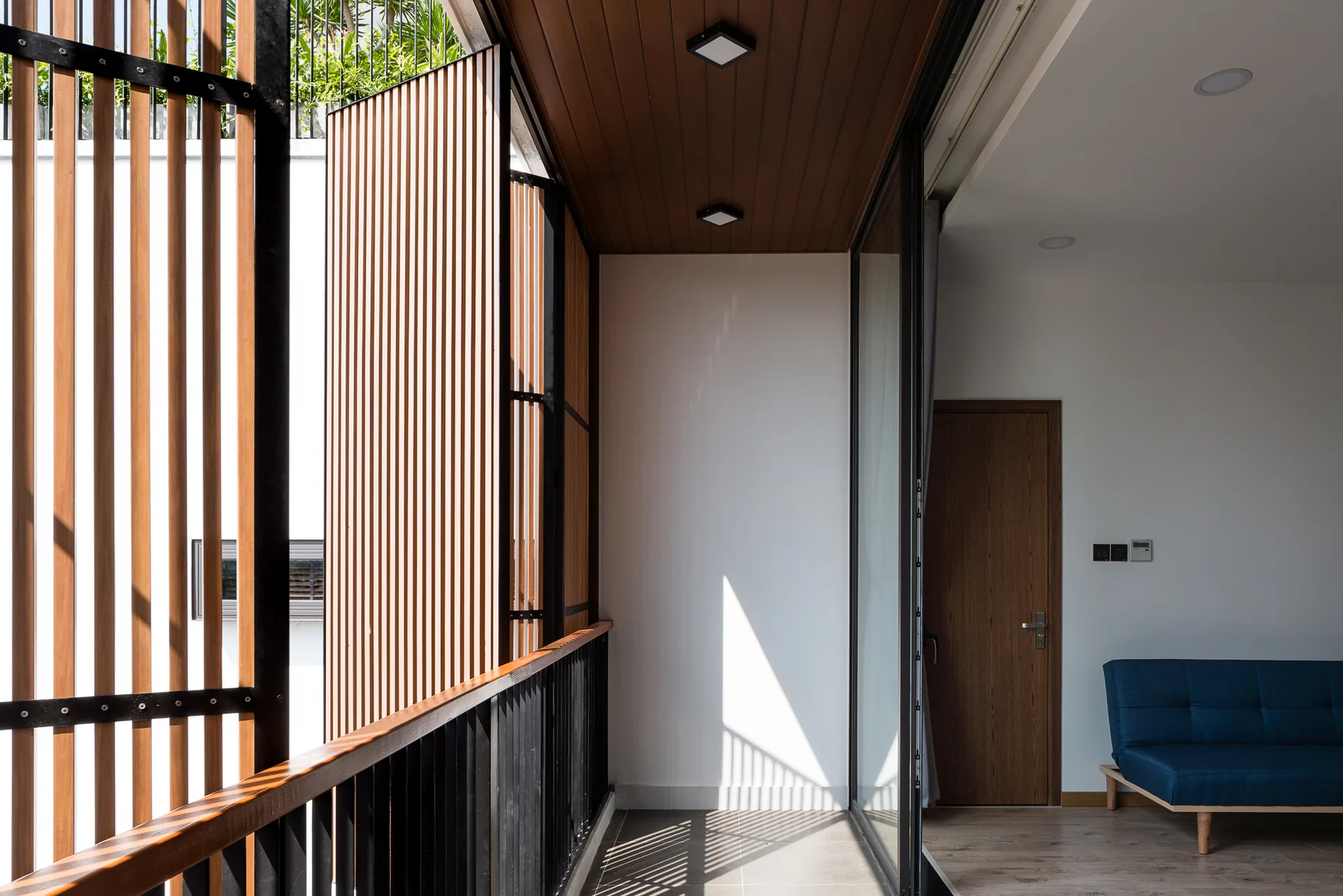 A modern balcony features vertical wood slat privacy screens, a timber plank ceiling, and a sliding glass door opening to an indoor room.