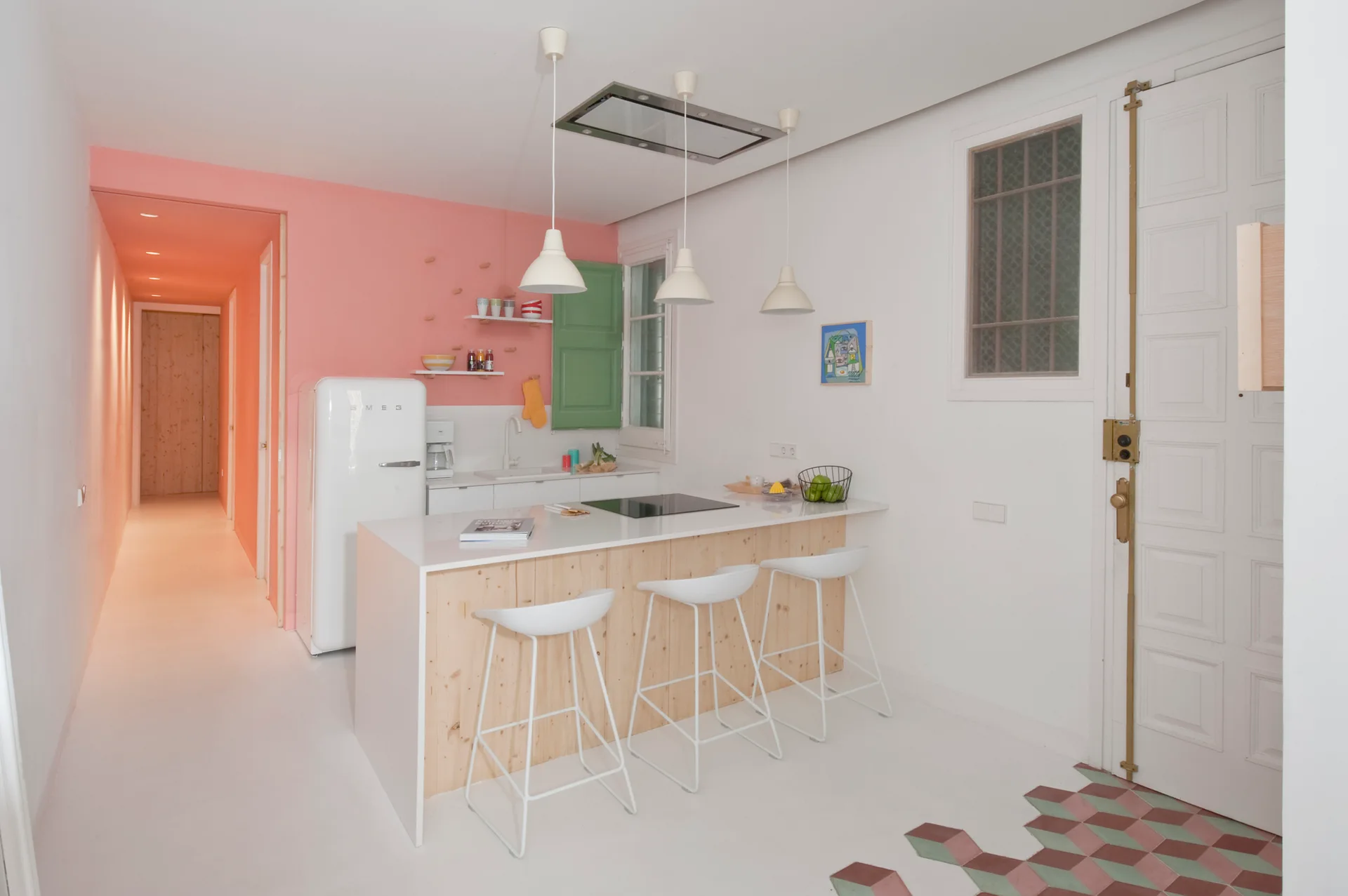 A modern kitchen features a pastel pink accent wall, a white kitchen island with light wood paneling, and three white bar stools.