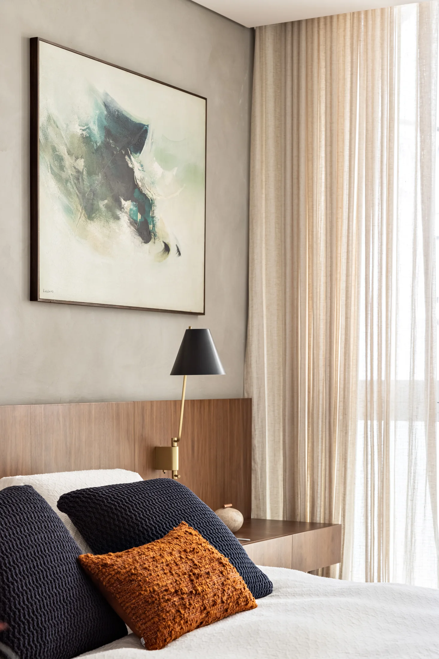 A close-up of a bed with blue and orange textured pillows set against a wood panel headboard, featuring a black wall sconce and abstract framed artwork.