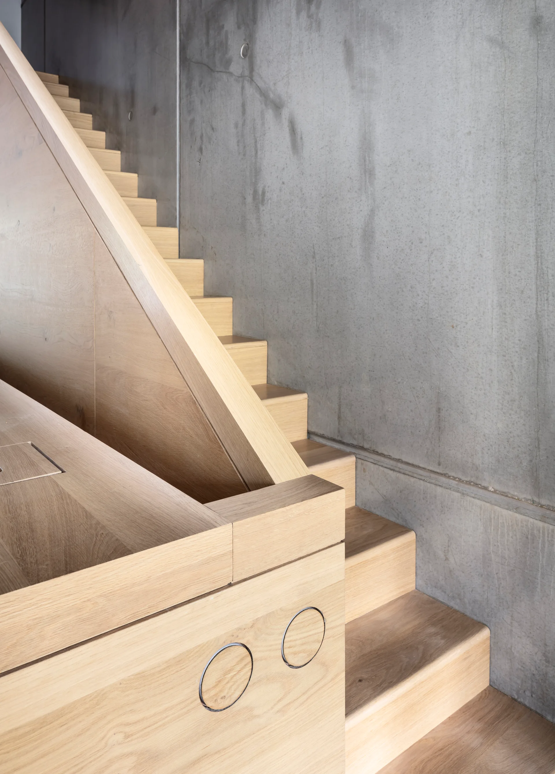 A close-up of a light wooden staircase and integrated wood paneling set against a grey poured concrete wall.