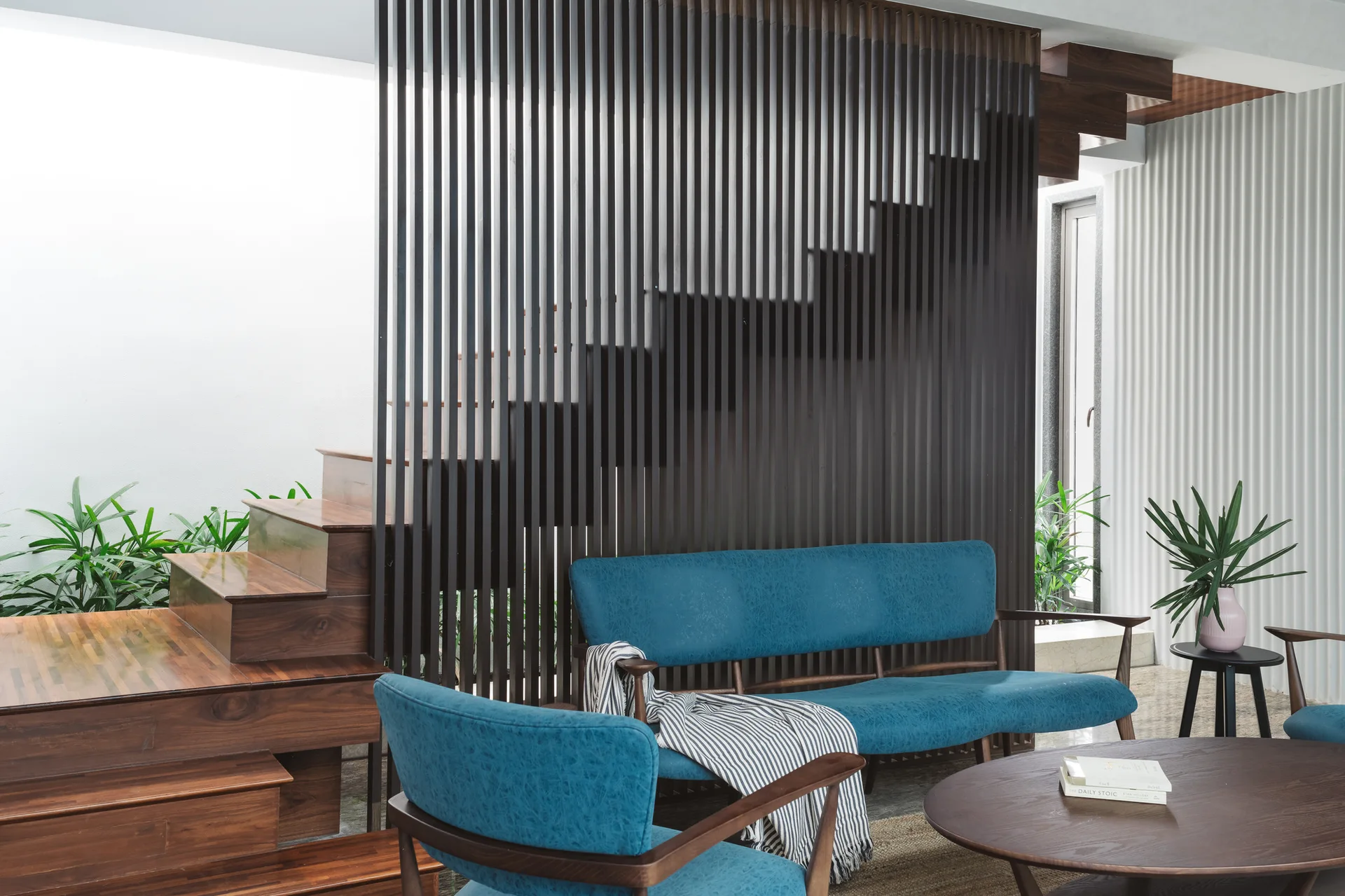 A blue upholstered sofa and armchair sit in front of a dark wood slatted room divider concealing a wooden staircase in a modern living space.
