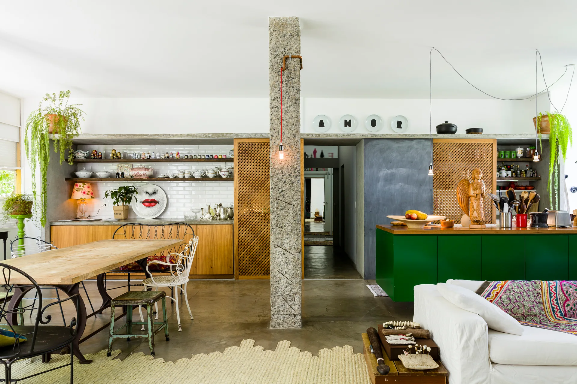 An eclectic open kitchen and dining area with a rustic stone pillar, green kitchen island, wood lattice screens, and a long wooden dining table.