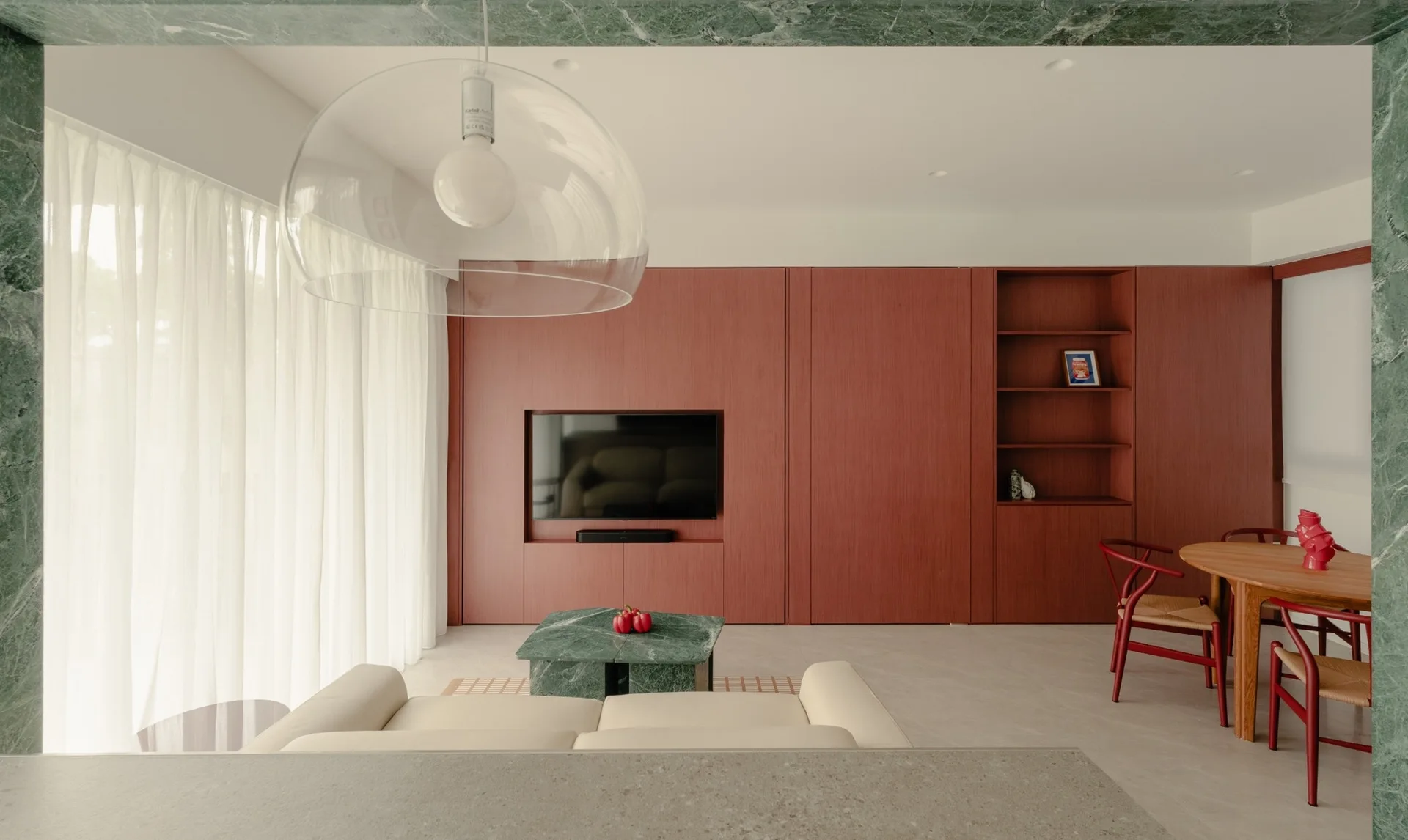 A modern living room features a cream sofa, a green marble coffee table, and an expansive wall of reddish-brown wood cabinetry.