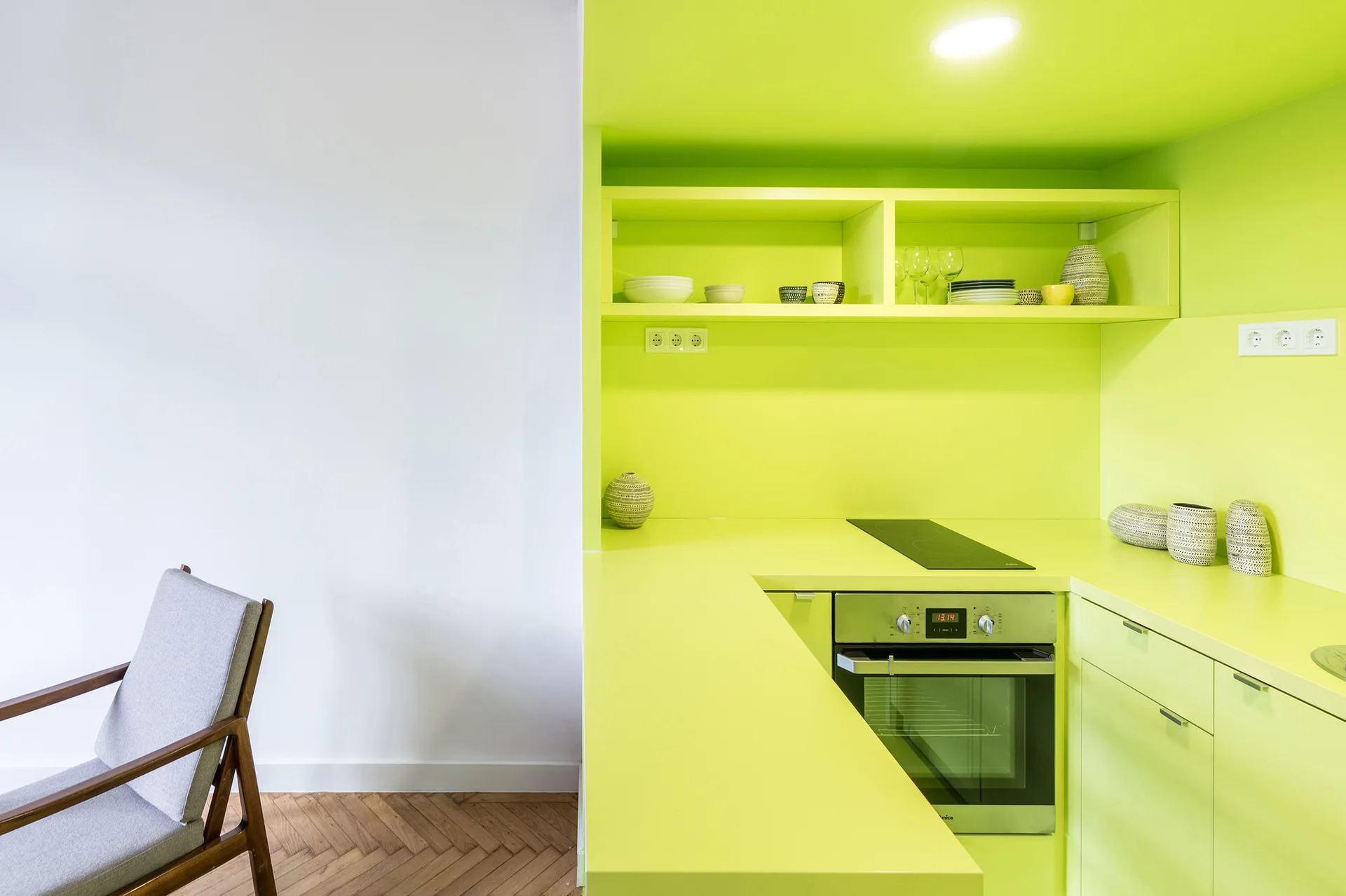 A minimalist kitchen area with bold lime green cabinets and countertops next to a neutral wall and a wood parquet floor.