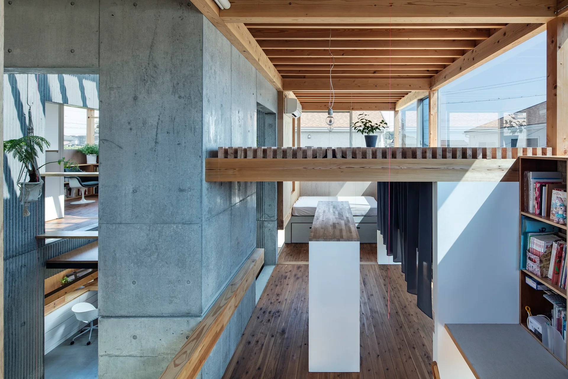 A multi-level modern interior featuring a large exposed concrete wall, warm wood ceiling beams, a built-in bookcase, and a low platform bed.