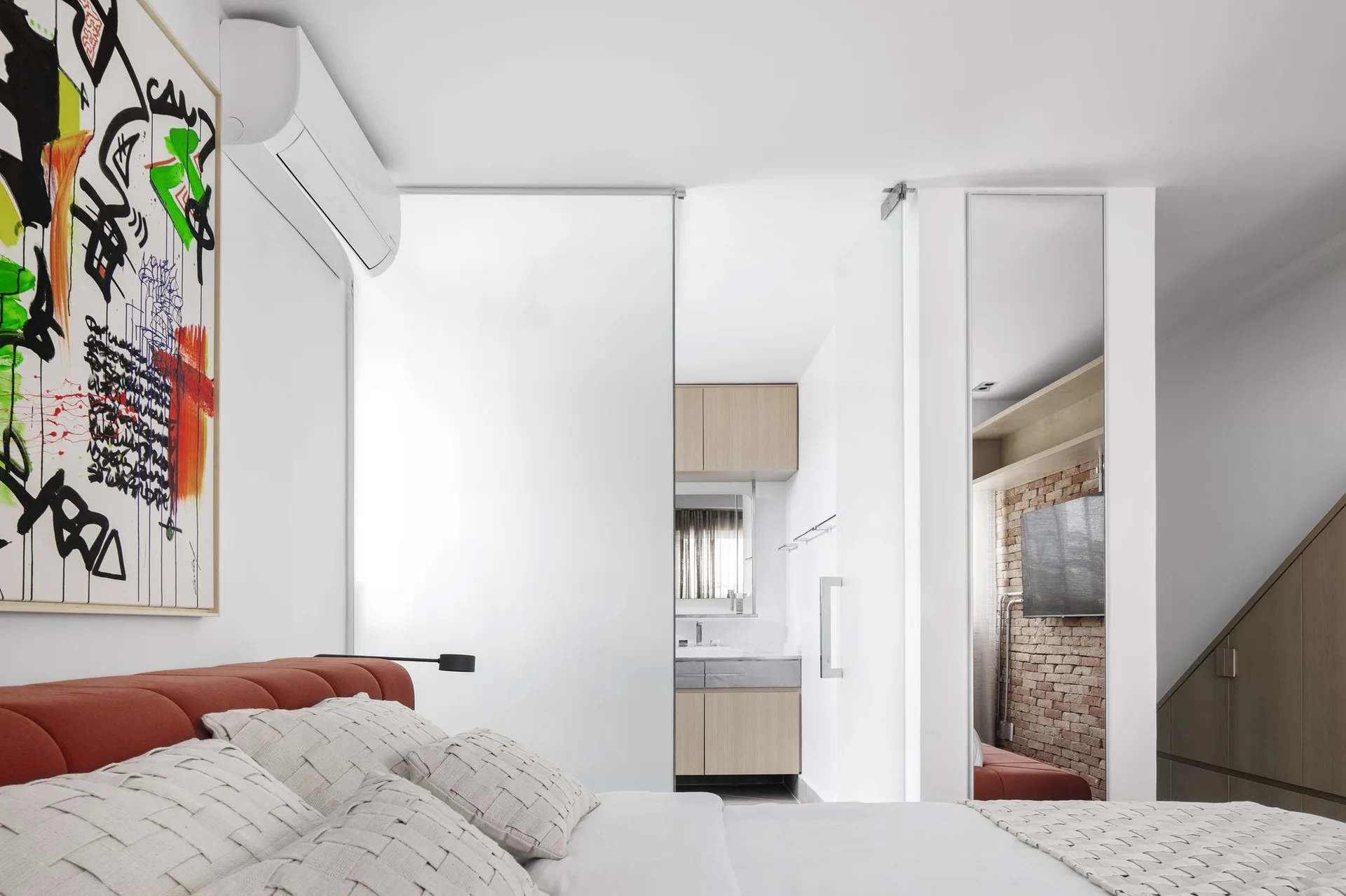 A modern bedroom features a terracotta tufted headboard, a white patterned comforter, and a frosted glass sliding door opening to an ensuite bathroom.