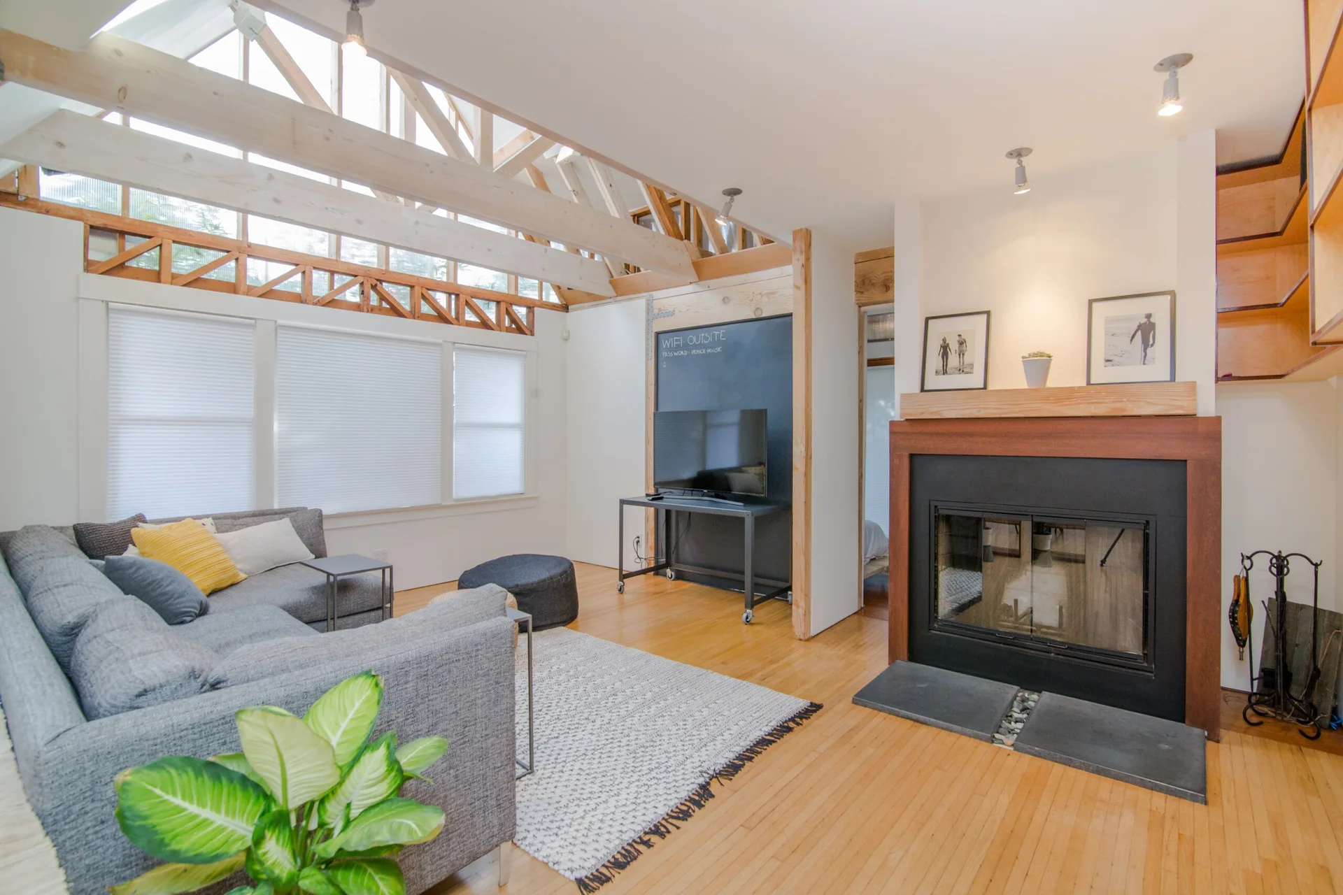 A contemporary living room featuring a gray sectional sofa, a fireplace with a wooden mantel, and high exposed wooden ceiling trusses.
