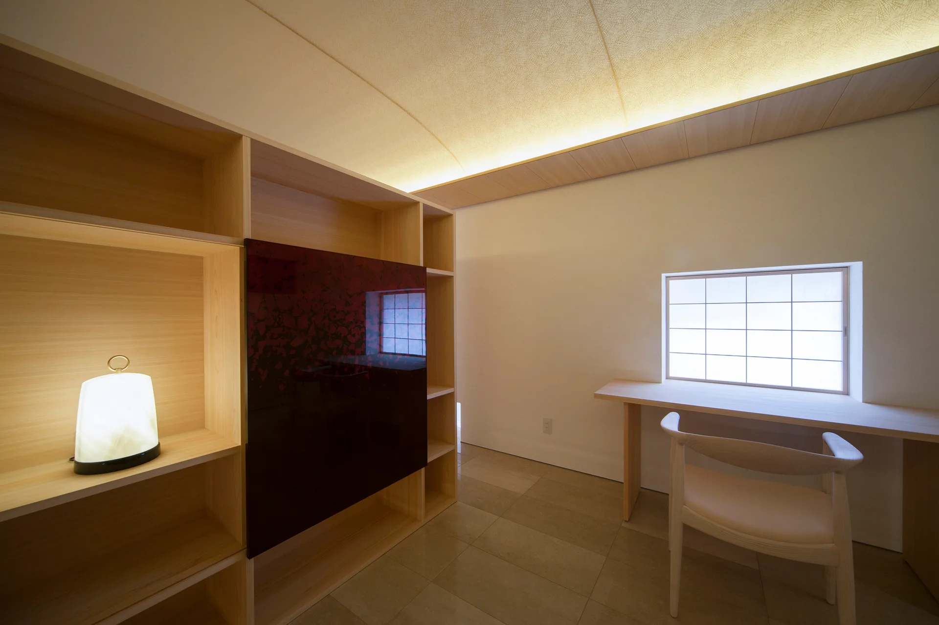 A minimalist home office features a light wood built-in desk under a grid window, built-in wooden shelving, and a curved ceiling with soft lighting.