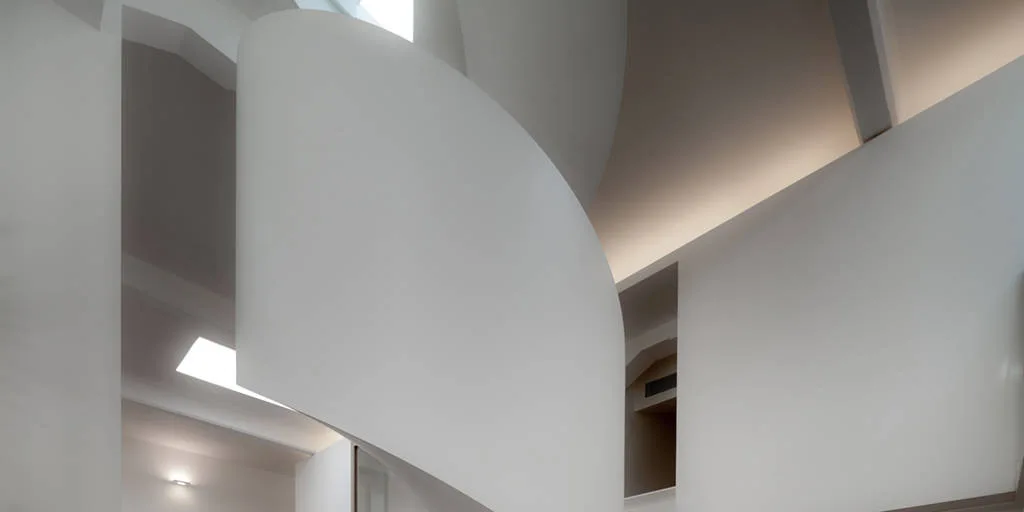 A minimalist interior featuring a sculptural white curved staircase lit by concealed recessed ceiling lights.