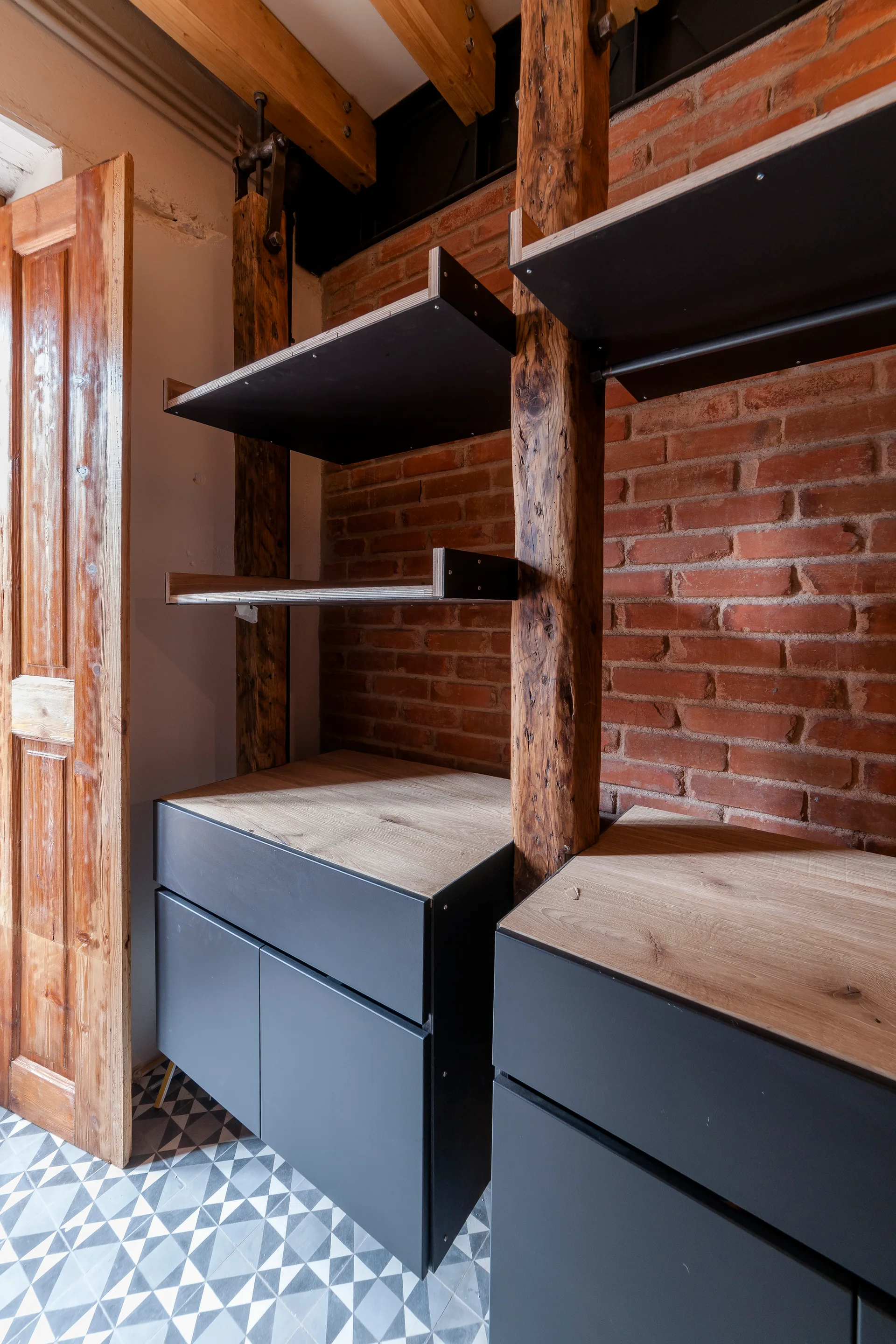 Matte grey base cabinets with wood tops and open shelving integrated with rough timber posts in front of an exposed red brick wall.