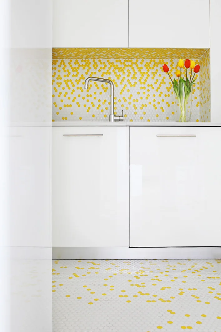 Modern kitchen with glossy white slab cabinets, a metal faucet, and scattered yellow and white hexagonal tiles on the backsplash and floor.