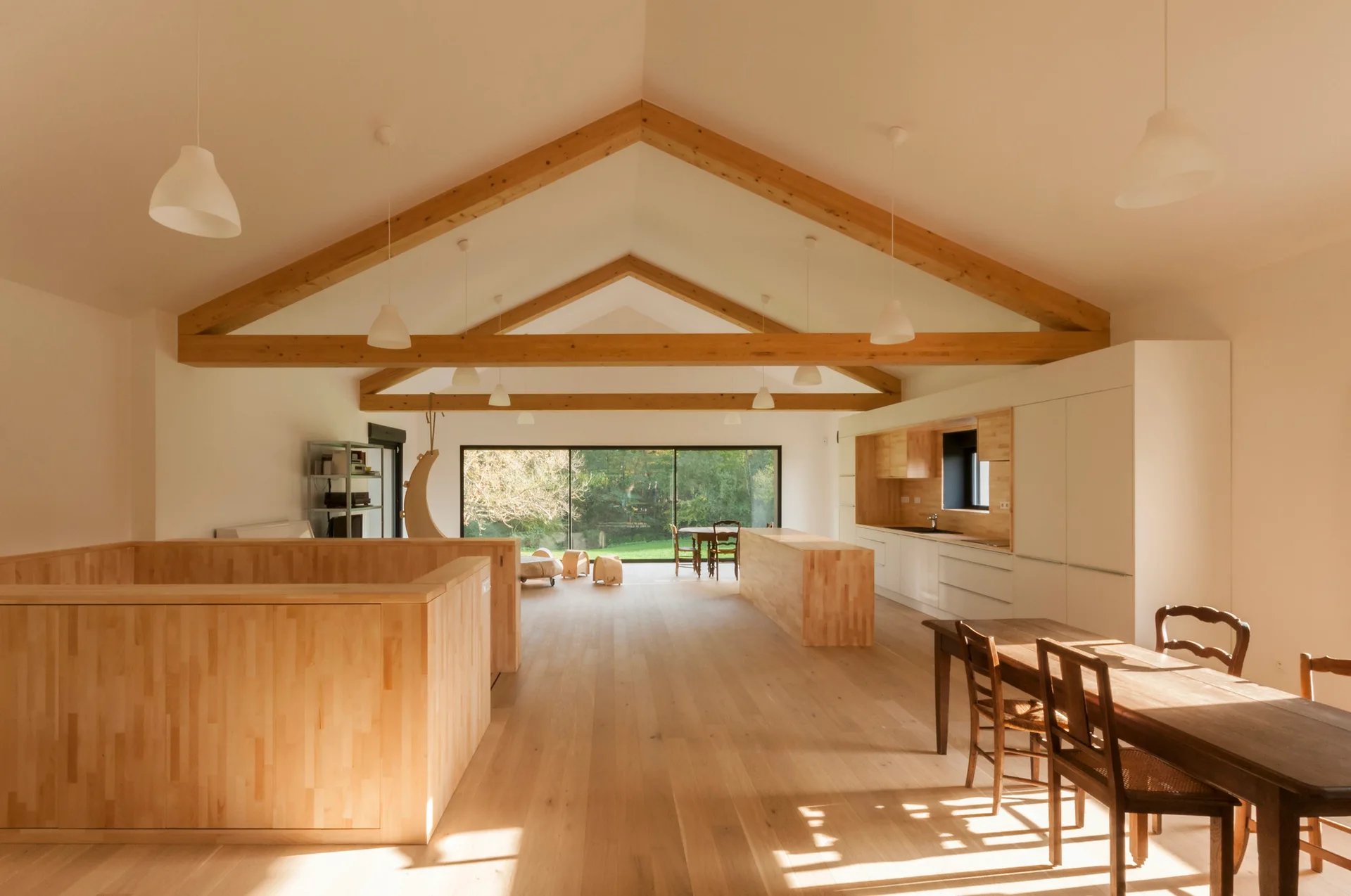 An open kitchen and dining area featuring vaulted ceilings with exposed wood beams, light wood flooring, white cabinetry, and a large glass sliding door.
