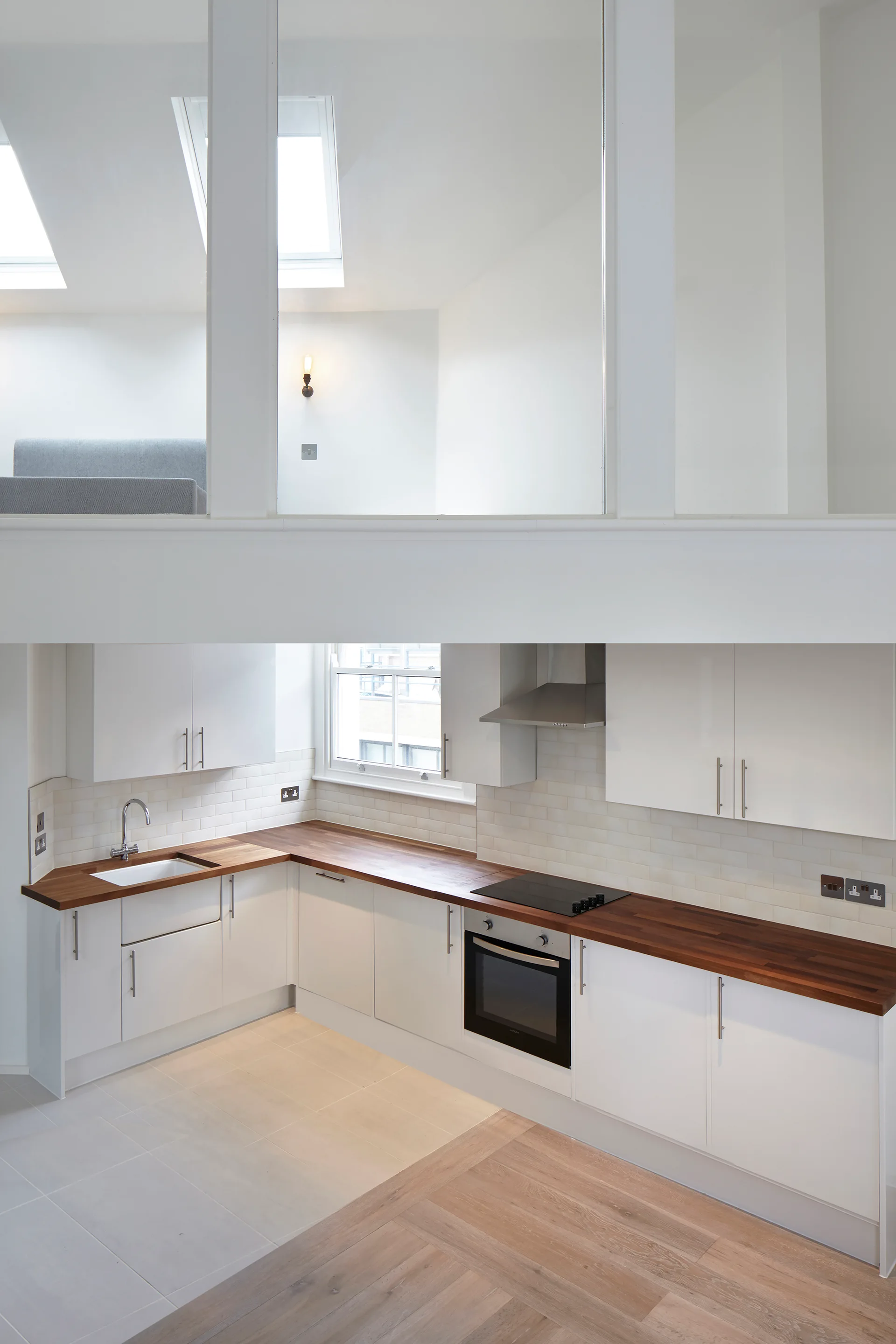 A modern kitchen with white cabinetry, wood-toned countertops, and white subway tile backsplash underneath a mezzanine balcony with skylights.