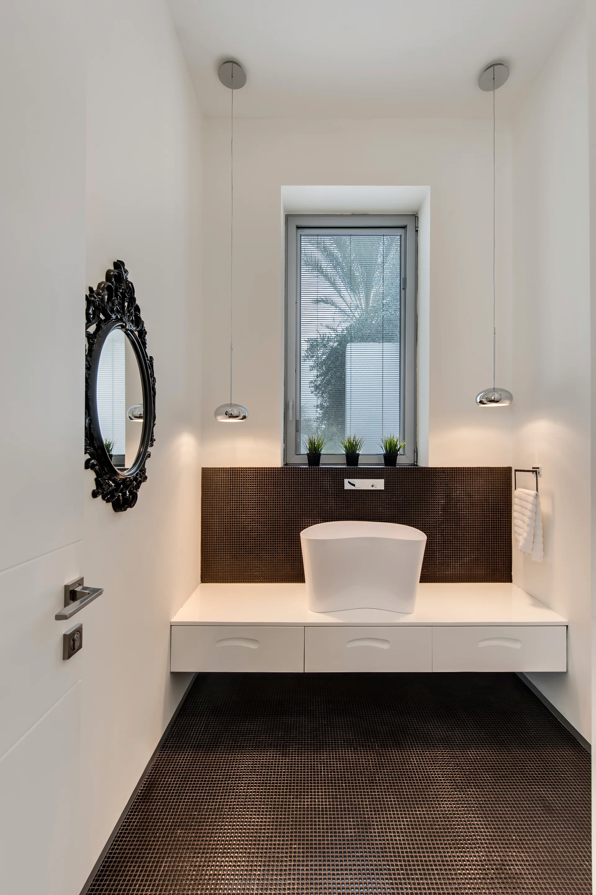 A minimalist powder room features a white floating vanity, a vessel sink, a dark mosaic tile backsplash, and an ornate black framed mirror.