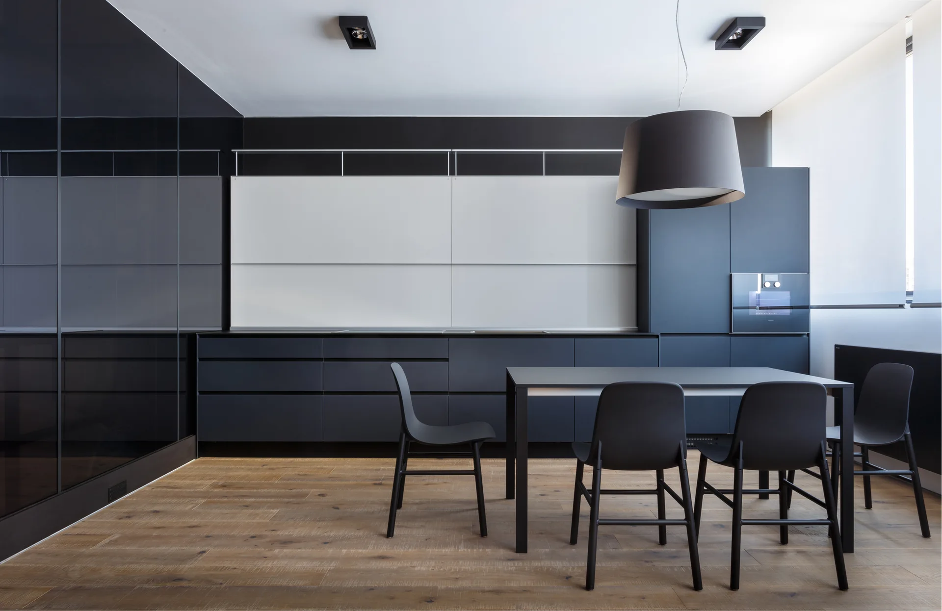 Minimalist kitchen featuring matte charcoal grey cabinetry, a black dining table with matching chairs, and light brown hardwood flooring.