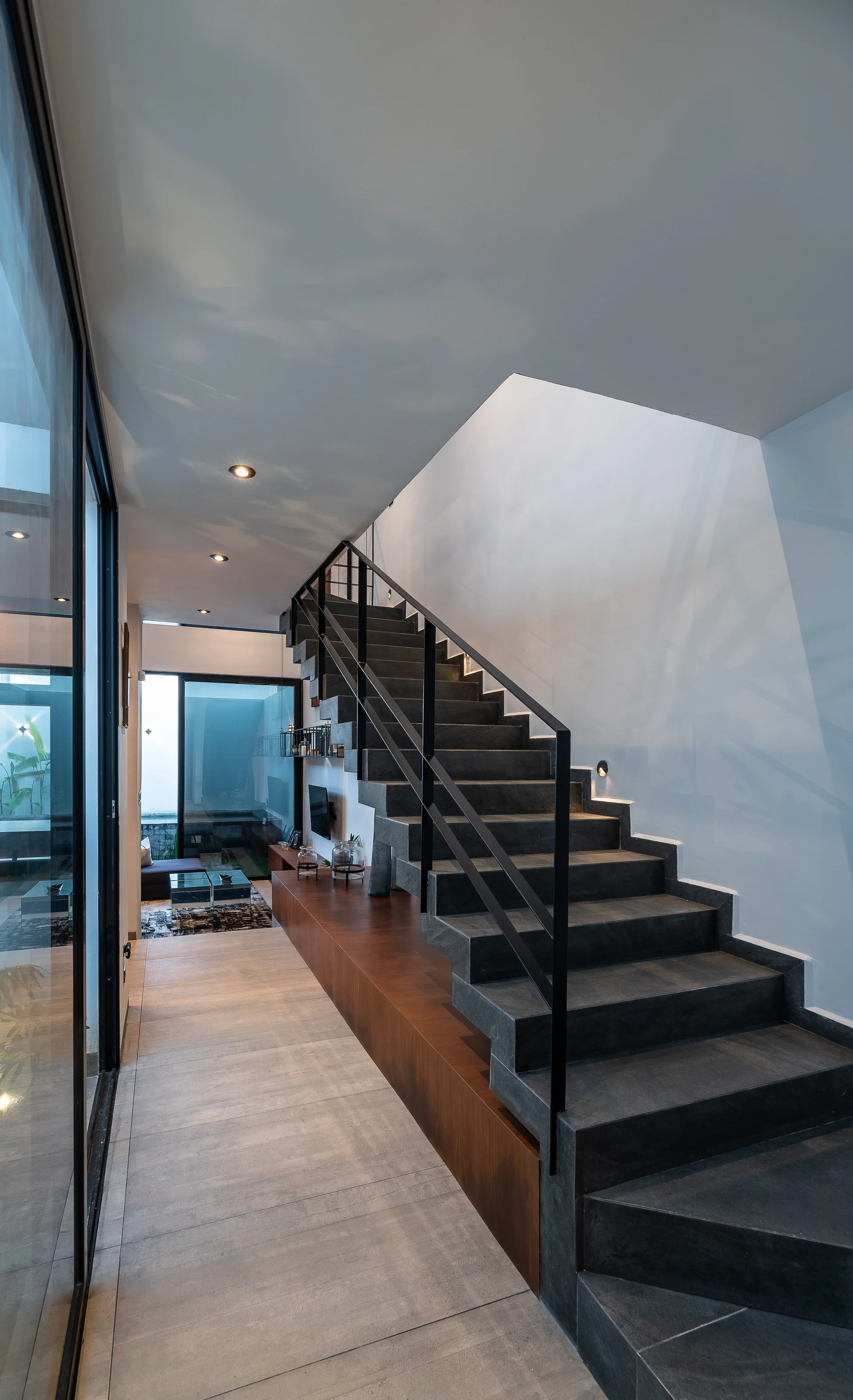 A modern minimalist hallway features a dark stone staircase with a black metal railing and a built-in wooden console base.