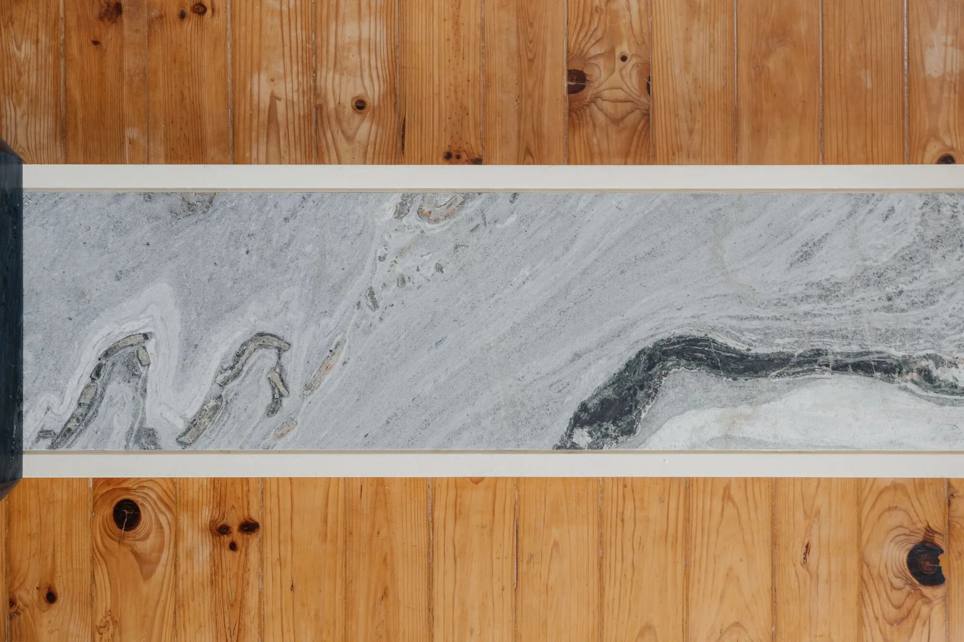 A close-up of natural wood flooring planks flanking a central grey marbled stone inlay strip.
