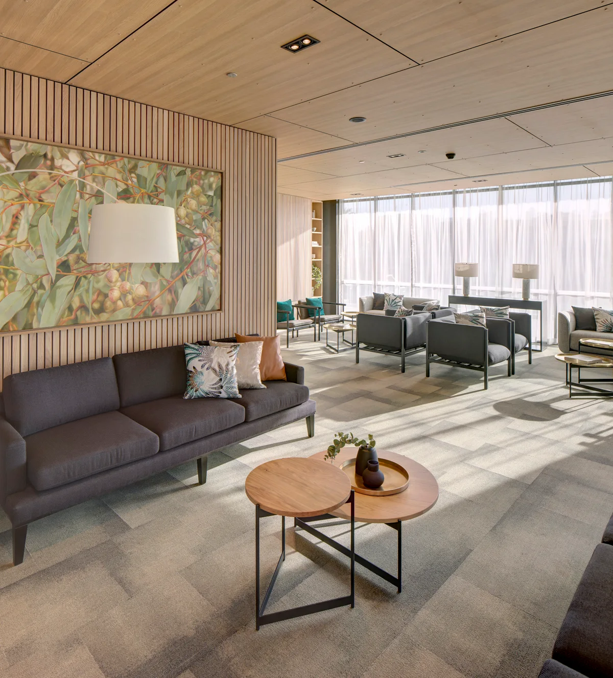 A contemporary lounge featuring a charcoal sofa, nested wooden coffee tables, and vertical wood-slatted walls under a matching paneled ceiling.