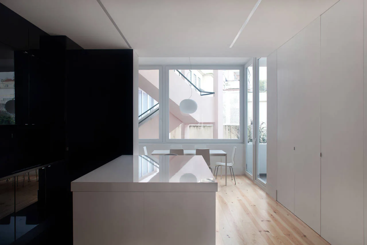 A minimalist kitchen features a glossy white island, a black lacquered wall panel, flat-panel white storage, and a light wood floor.
