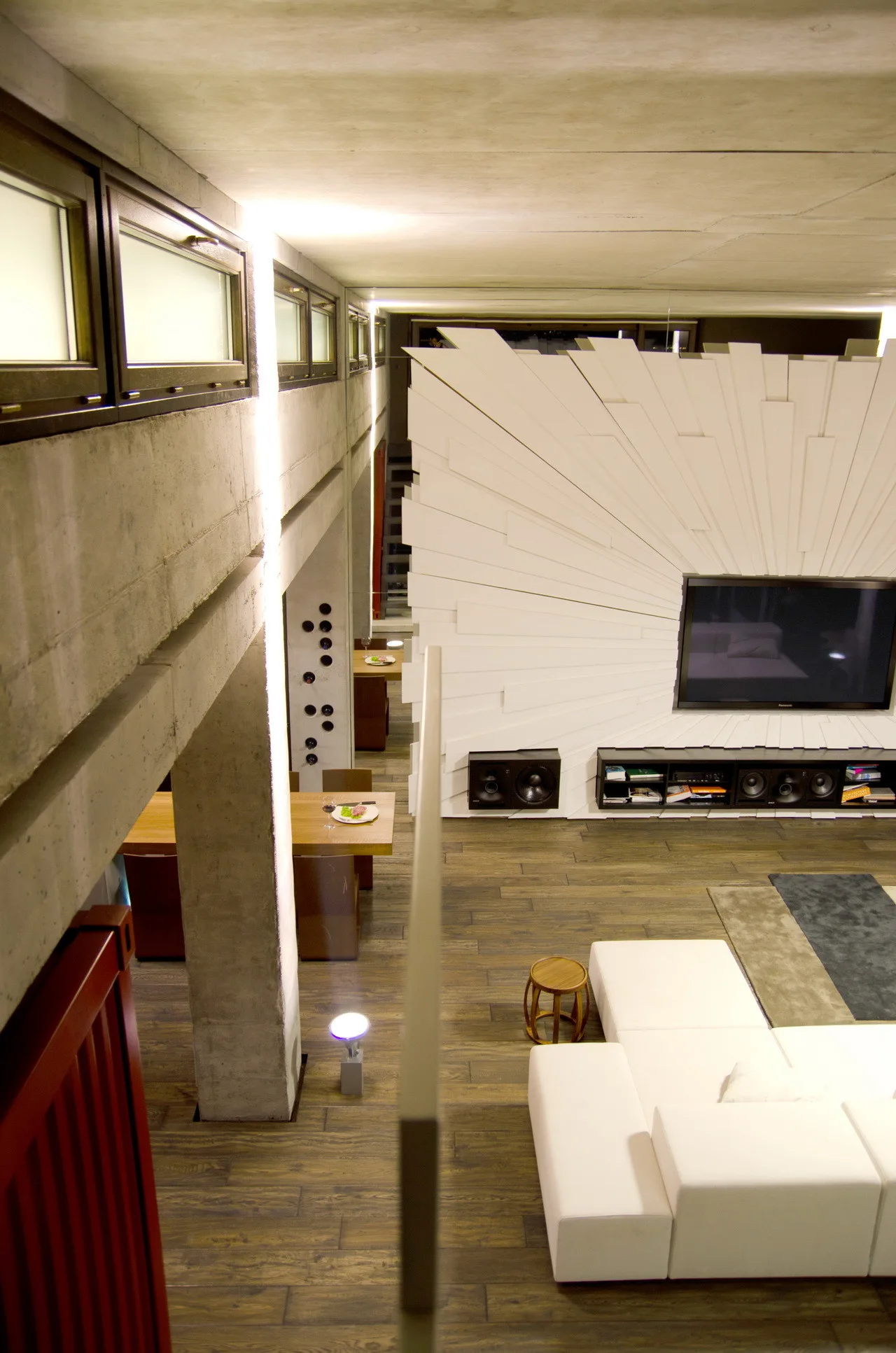 A high-angle view of a contemporary living room featuring a white modular sectional, a large white sunburst sculptural wall panel, and concrete columns.
