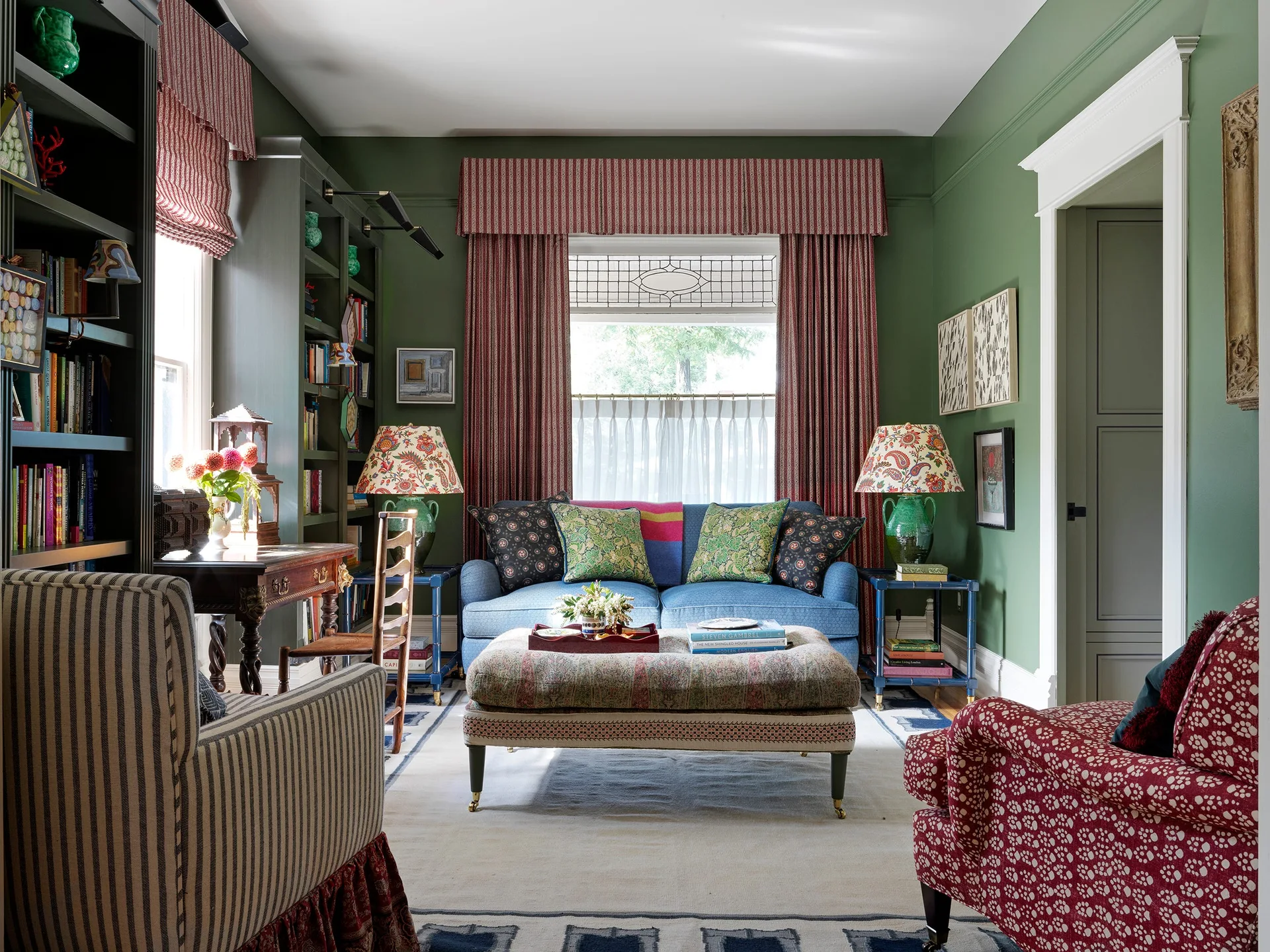 A traditional living room with green walls, a blue upholstered sofa, striped drapes, and a patterned ottoman.