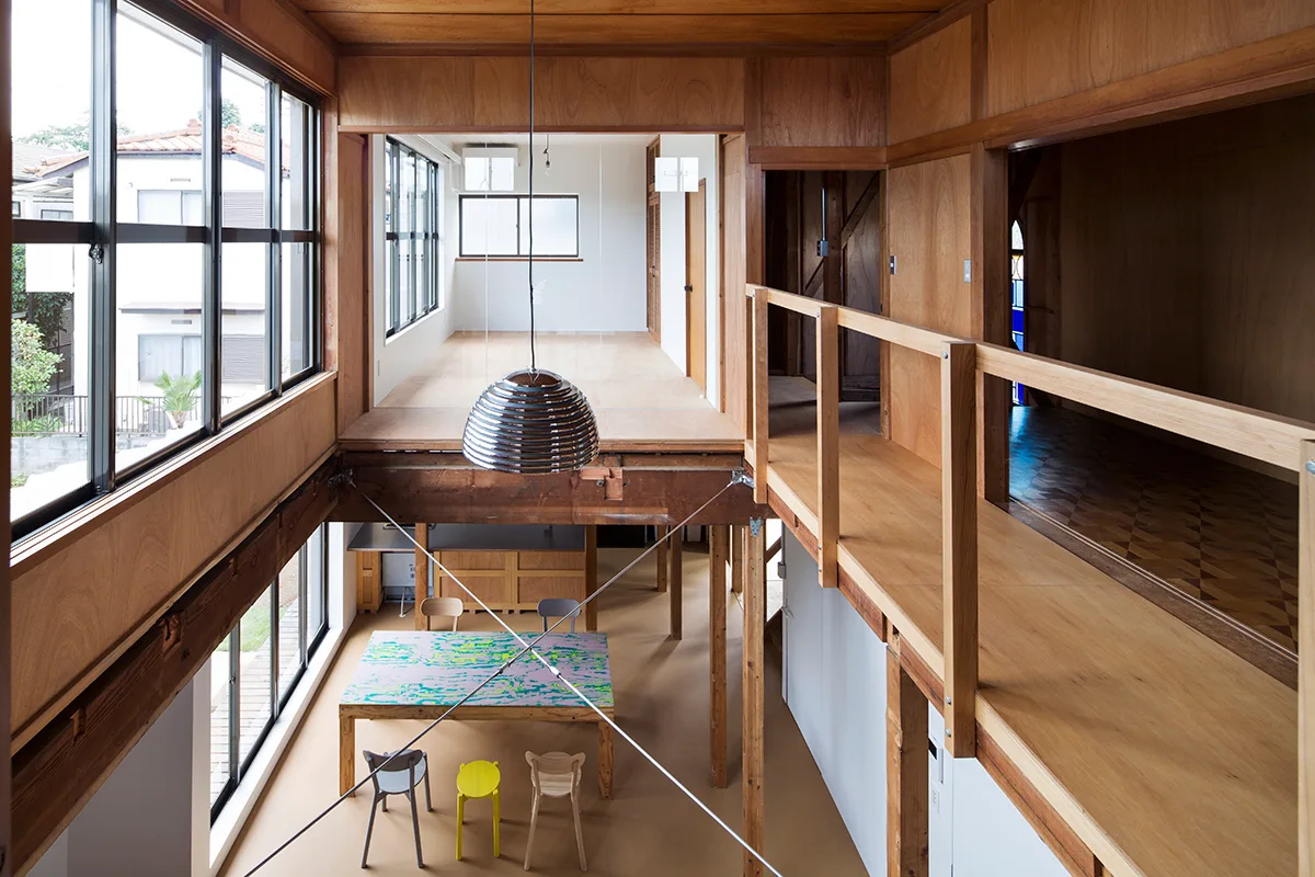 A split-level residential interior with natural wood wall paneling, a wooden walkway on the upper level, and a dining table on the lower floor.