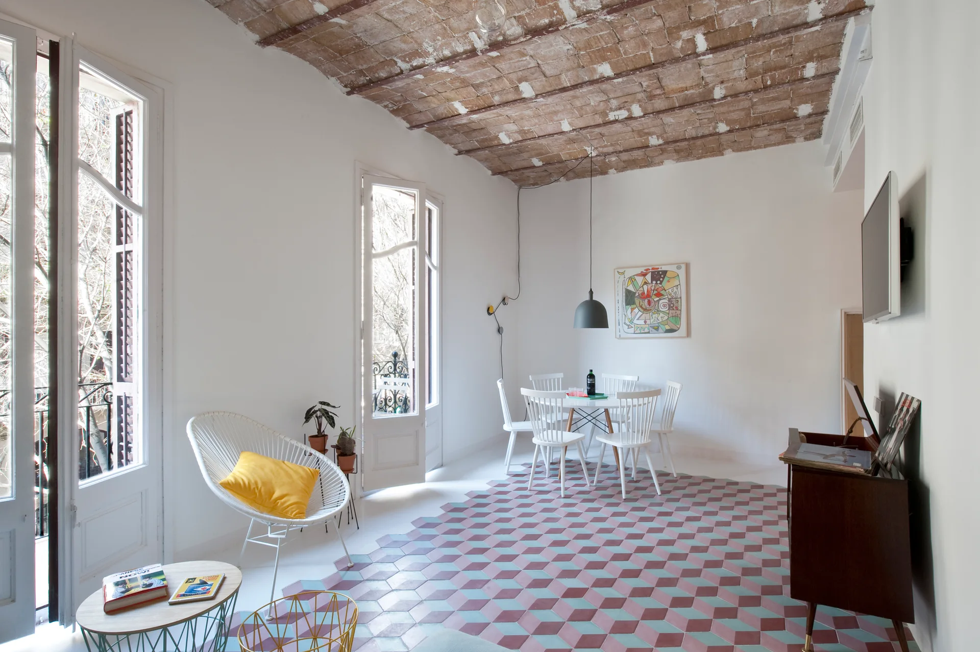 A bright dining space with a barrel-vaulted brick ceiling, white furniture, and a multi-colored geometric cube tile floor.