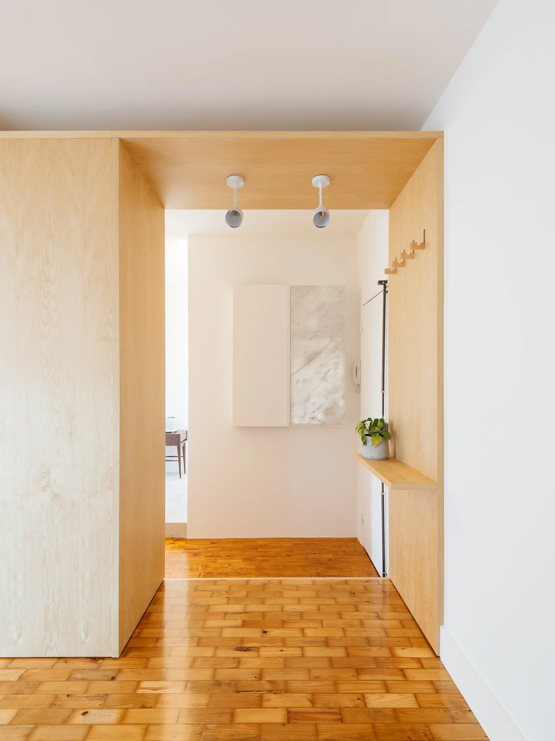 A minimalist hallway features a light wood portal with integrated wooden coat hooks, a small shelf, ceiling spotlights, and a wood floor.