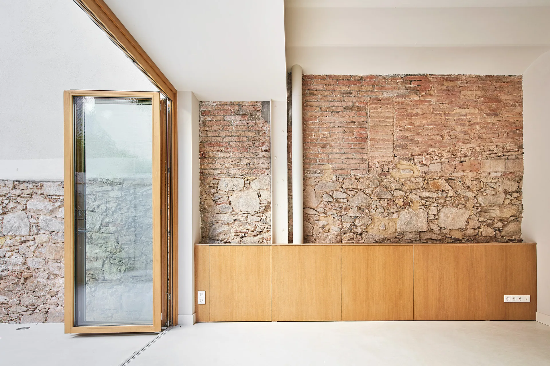 An interior room featuring an exposed brick and stone wall above built-in wood cabinets and a large wooden glass door opening to a patio.