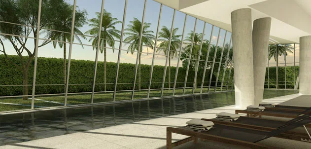 A modern indoor pool deck featuring lounge chairs arranged next to a large slanted glass curtain wall looking out at palm trees.